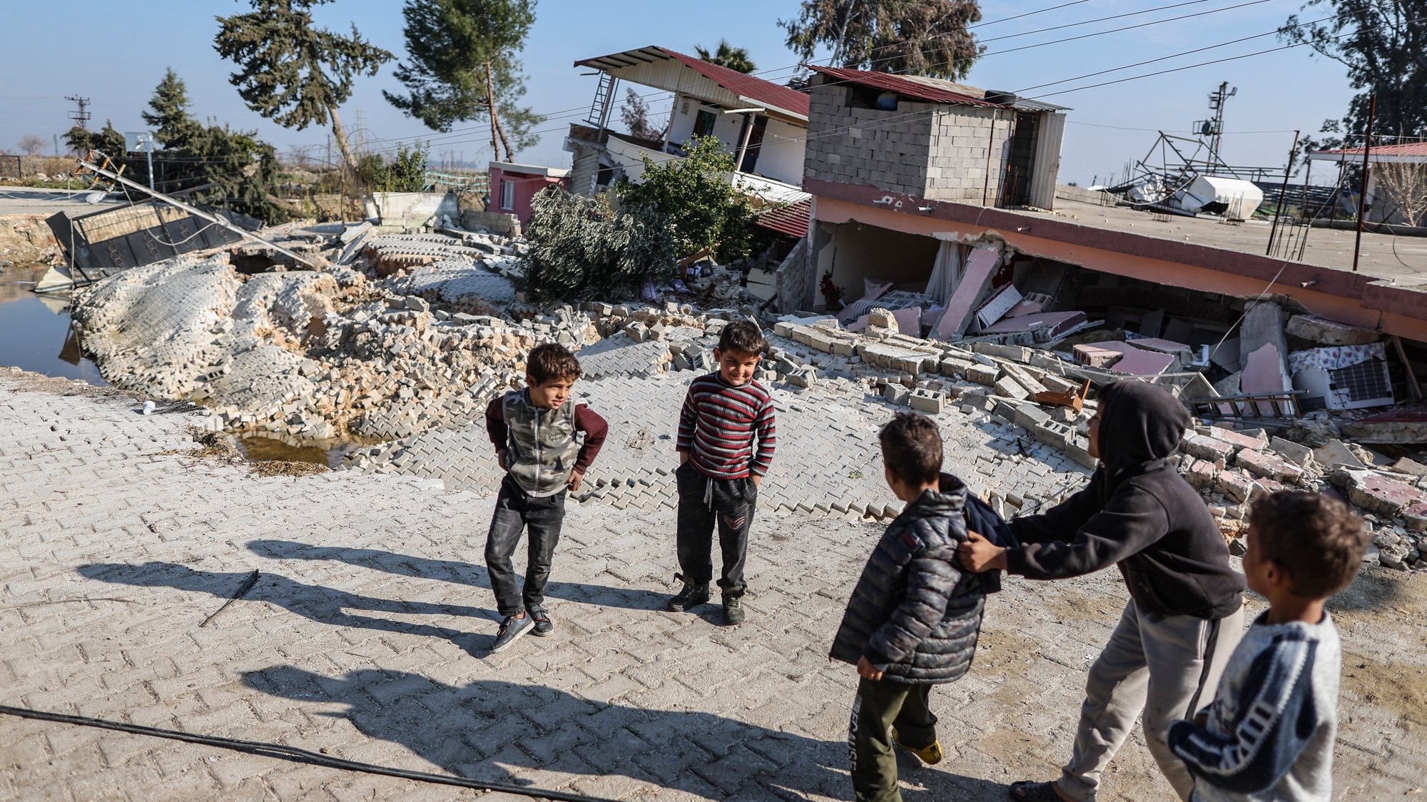 epa10483167 Children play in front of buildings collapsed by a fault line in Demirkopru village, Hatay district, Turkey 22 February 2023. The fault line follows a 6.3-magnitude earthquake, according to U.S. Geological Survey, that hit the Syria-Turkey border on 20 February, weeks after a 7.8-magnitude earthquake hit the region on 06 February, killing more than 46,000 people.  EPA/ERDEM SAHIN