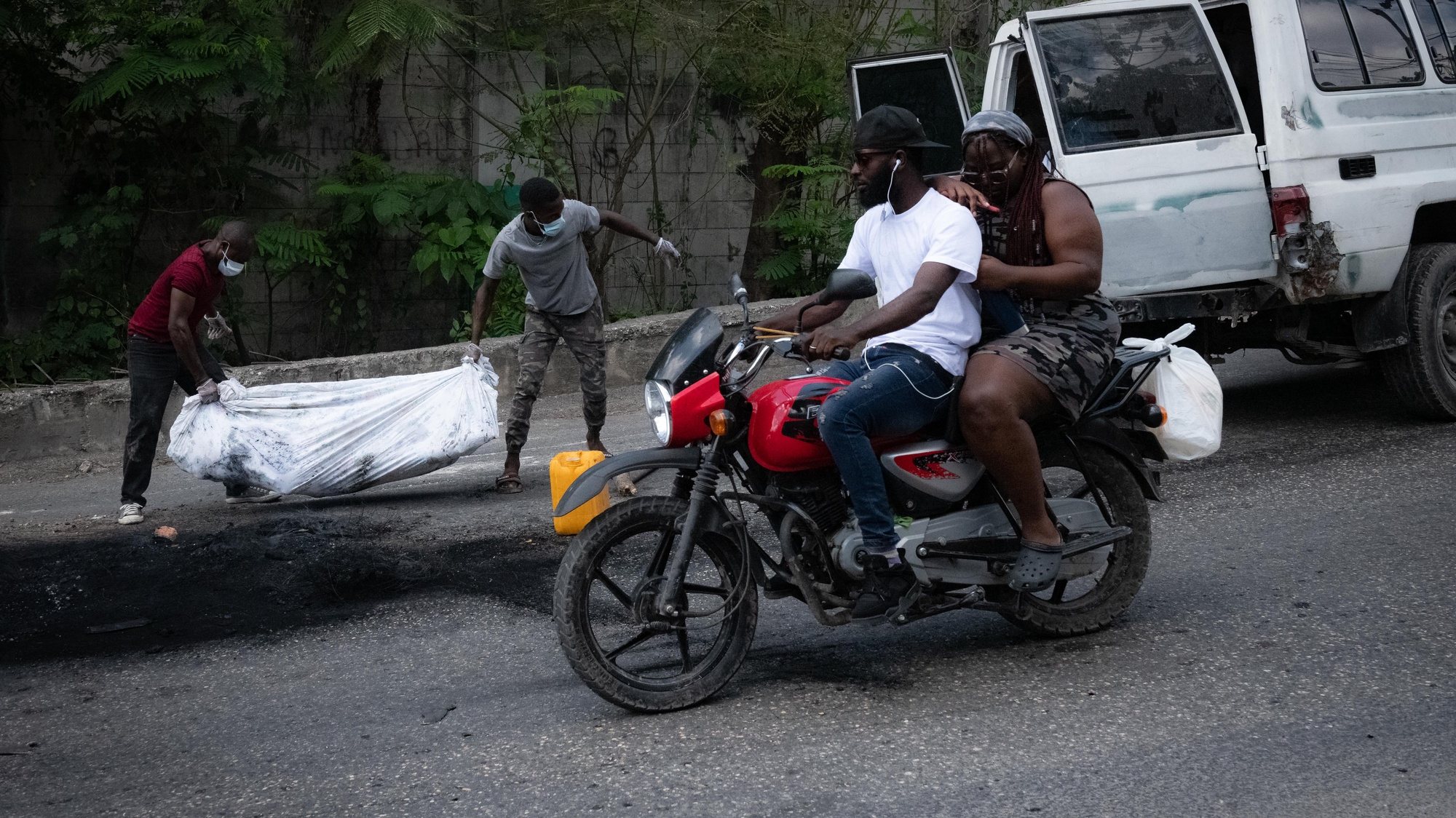 epa10605580 Two men carry the cremated body of a person in Port-au-Prince, Haiti, 02 May 2023. At least five people were killed on 02 May 2023 by the population in Petion-ville, Port-au-Prince, for being alleged members of the Ti Makak armed group, dismantled a few weeks ago by the National Police.  EPA/Johnson Sabin
