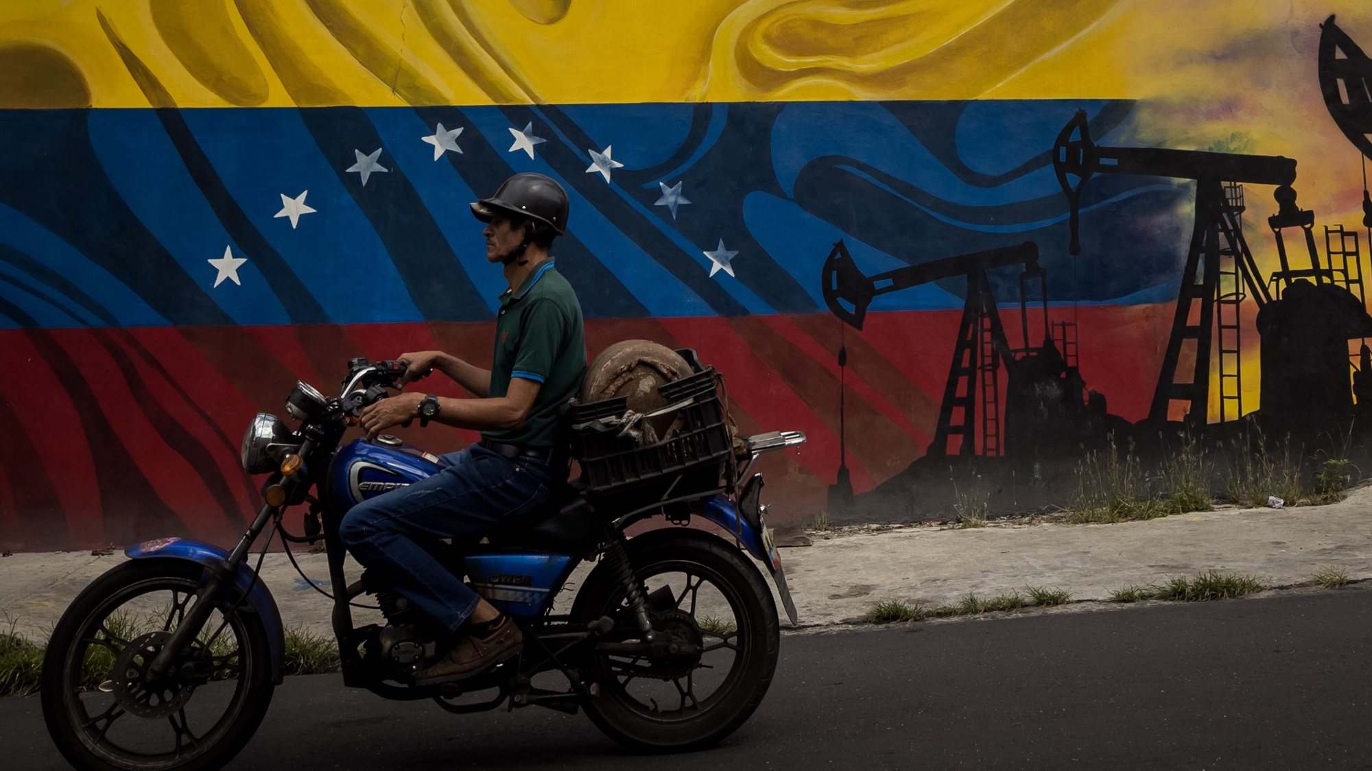 epa10778859 A motorcyclist passes a mural at the Complex MinPetroleo - Petroleos de Venezuela S.A (Pdvsa), in Caracas, Venezuela, 27 July 2023 (issued 31 July 2023). The goose that lays the golden eggs of Venezuela, the oil industry, has been on the table in recent weeks, when candidates for the opposition primaries have debated whether or not to privatize it, an option that some applicants have as a goal,  reach the Venezuelan presidency post.  EPA/MIGUEL GUTIERREZ