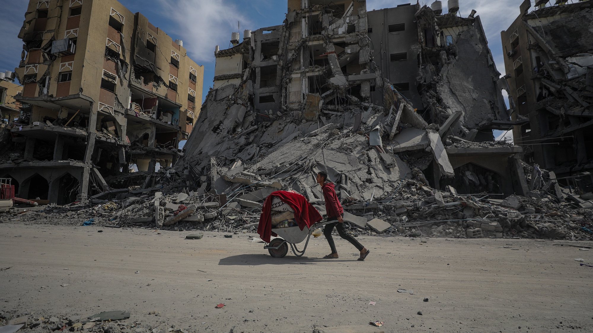 epaselect epa11220424 A Palestinian man pushes a wheelbarrow past the rubble of destroyed houses at Hamad towers city following an Israeli military operation in Khan Younis town, southern Gaza Strip, 14 March 2024. More than 31,000 Palestinians and over 1,300 Israelis have been killed, according to the Palestinian Health Ministry and the Israel Defense Forces (IDF), since Hamas militants launched an attack against Israel from the Gaza Strip on 07 October 2023, and the Israeli operations in Gaza and the West Bank which followed it.  EPA/MOHAMMED SABER