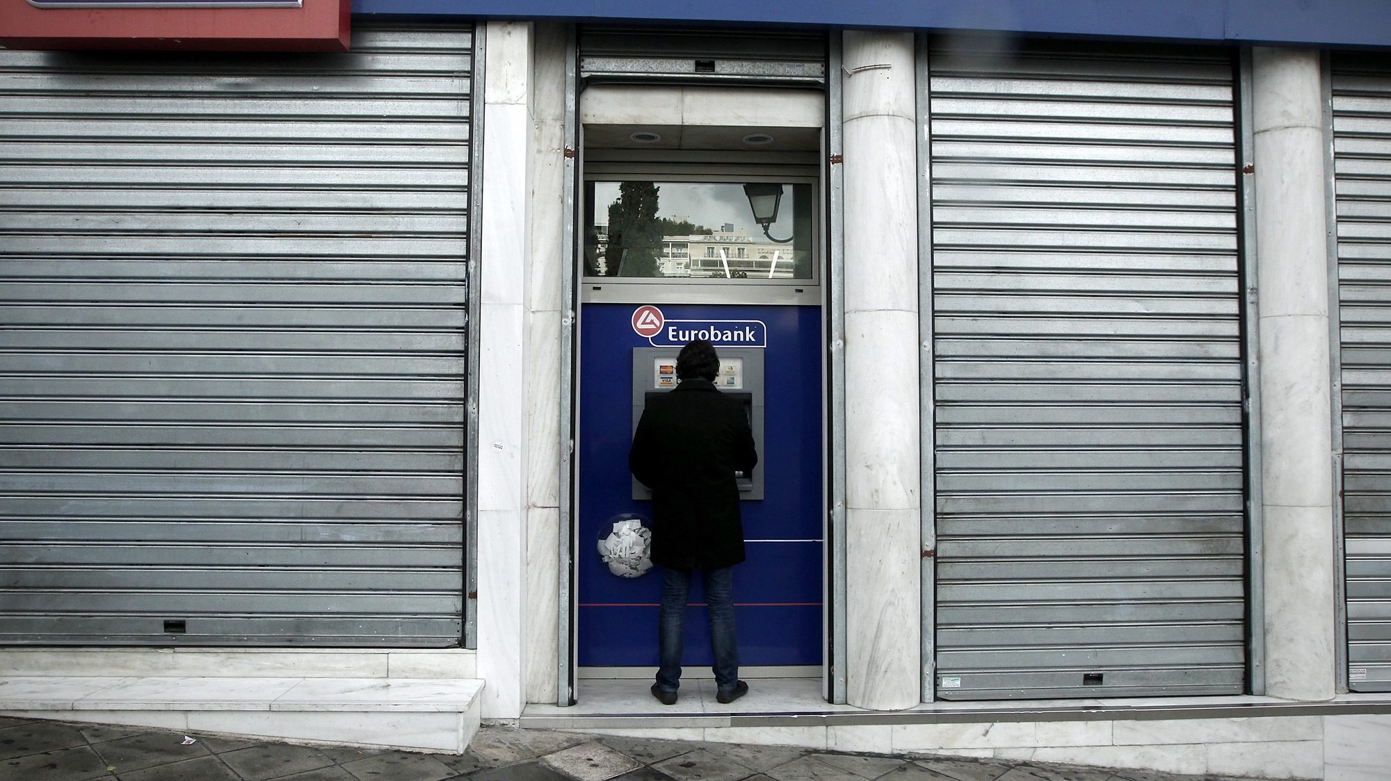 epa03526006 A man uses an ATM of a closed branch of Eurobank in central Athens, Greece, 06 January 2013. The head of the European Investment Bank (EIB) said it would take Greece decades to recover from its financial crisis and criticized the efforts of European politicians.  EPA/ALKIS KONSTANTINIDIS