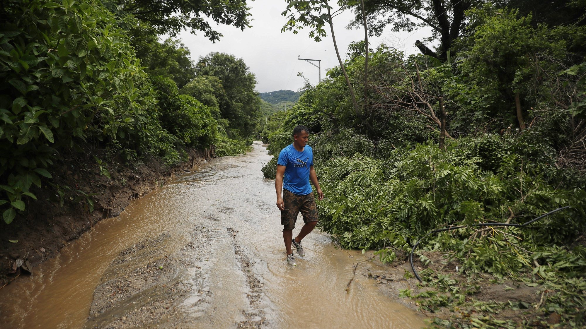 epa11430993 A man walks along a path flooded due to heavy rains in Soyapango, El Salvador, 21 June 2024 (issued 22 June 2024). A Salvadoran family spent the night in a boat after the collapse of an earthen dam destroyed their home and heavy rains threatened more landslides, adding to the more than 3,800 people who have had to be evacuated because of the rains that have lashed El Salvador since last week and have left at least 19 people dead and two missing.  EPA/Rodrigo Sura