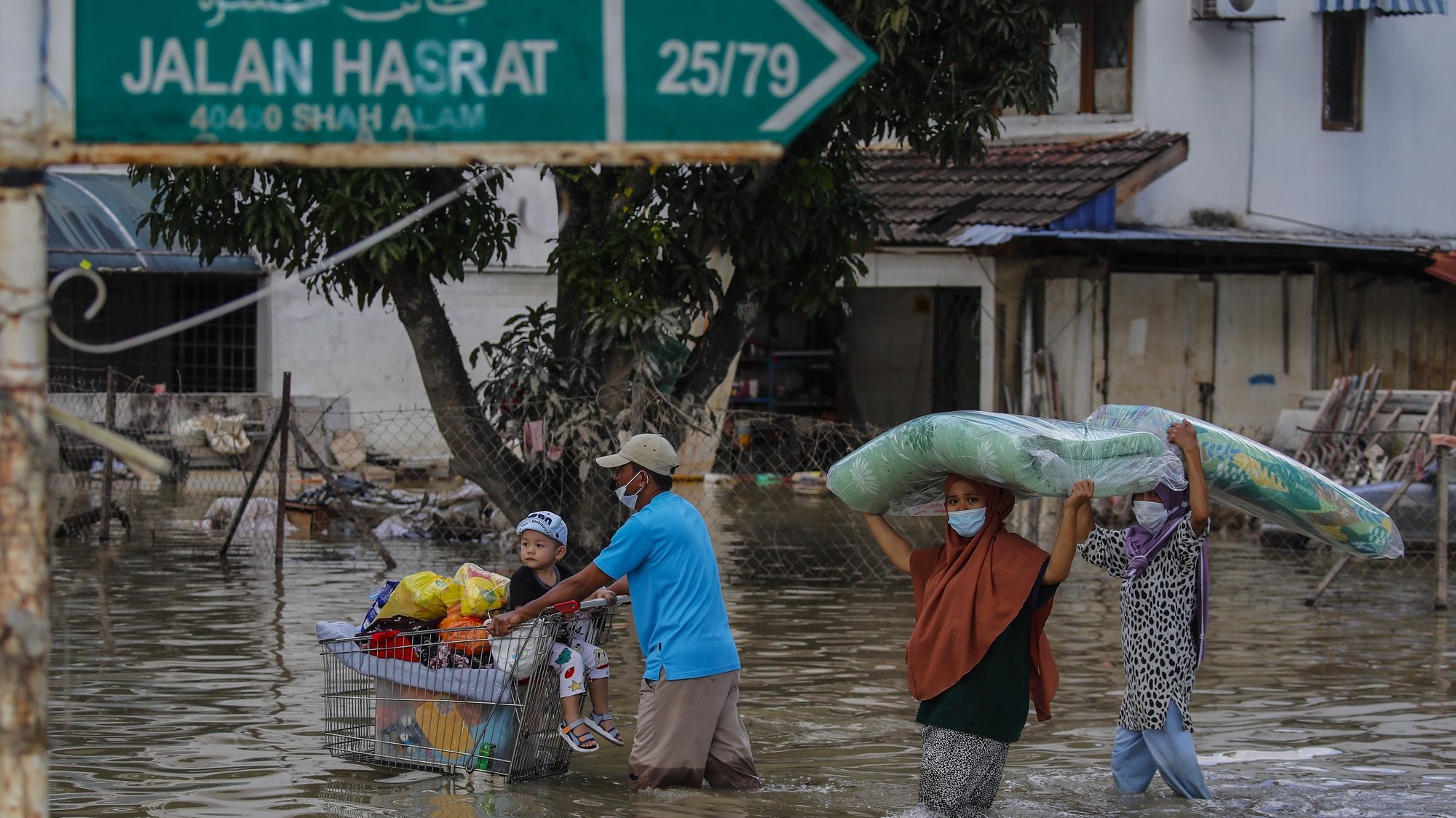 epaselect epa09652236 A man (L) pushes a trolley cart with his son and belongings, as others family members carry a mattress, after floods struck Taman Sri Muda, Shah Alam district, some 40km from Kuala Lumpur, Malaysia, 21 December 2021. Flooding in Malaysia leaves 17 dead and more than 70,000 displaced after several Malaysian states has been struck by floods caused by two days of heavy rain with many trapped in their vehicles and homes.  EPA/FAZRY ISMAIL