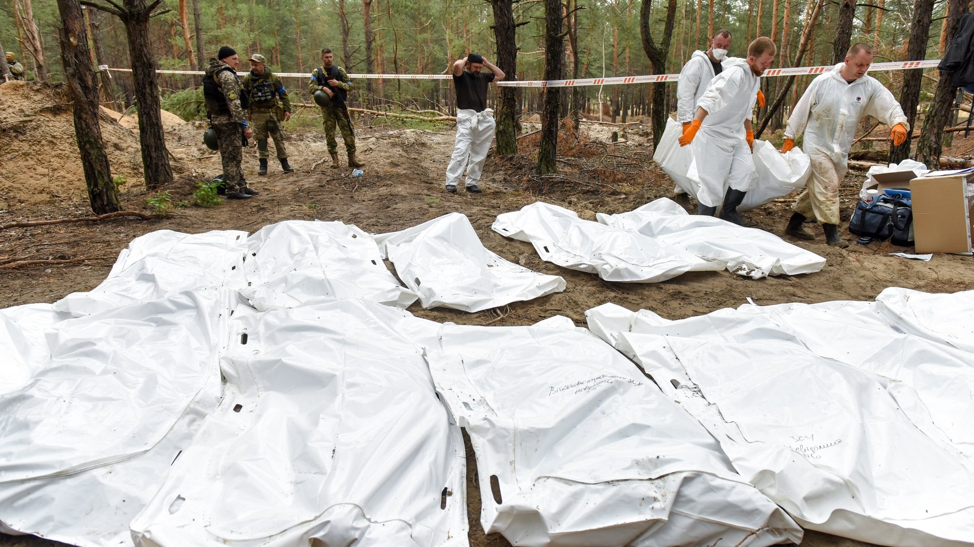 epa10188706 Ukrainian servicemen stand near workers carrying bodies that were were unearthed from graves in Izyum, Kharkiv region, northeastern Ukraine, 16 September 2022. A mass burial site was found after Ukrainian troops recaptured the town of Izyum. According to the head of the investigative department of the police of the Kharkiv region, the burial site, one of the largest in a recaptured city so far, counts more than 440 separate graves. The Ukrainian army pushed Russian troops from occupied territory in the northeast of the country in a counterattack. Kharkiv and surrounding areas have been the target of heavy shelling since February 2022, when Russian troops entered Ukraine starting a conflict that has provoked destruction and a humanitarian crisis.  EPA/OLEG PETRASYUK  EPA-EFE/OLEG PETRASYUK