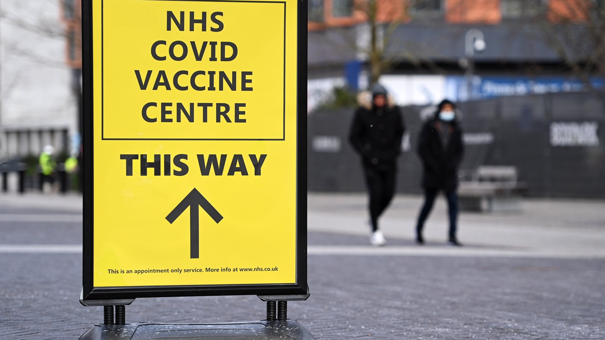 epa09001299 People walk past a sign to a Covid-19 vaccination centre in London, Britain, 10 February 2021. British Vaccines Minister Nadhim Zahawi has stated he was confident the NHS would be able to reach the target of immunising all those over the age of fifty by May. Some twelve million people across the UK have already received their first dose of a Covid-19 vaccine.  EPA/ANDY RAIN