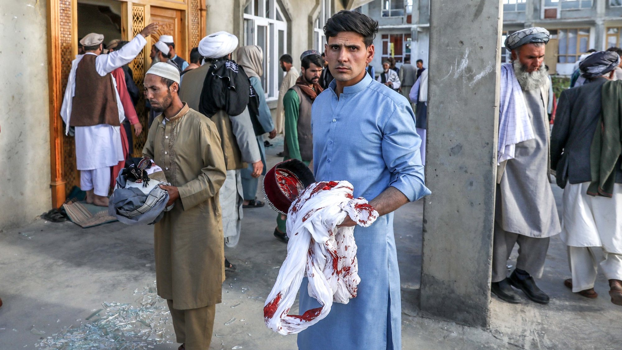 epa09199608 Afghan men hold the belongings of worshippers at the scene of an attack that targeted a mosque in the outskirt of Kabul, Afghanistan, 14 May 2021. At least 12 people were killed and 15 others wounded after a planted bomb exploded during Friday prayers inside Haji Bakhshi Mosque in Qala-e-Murad Bek area in Shakardara district of Kabul.  EPA/HEDAYATULLAH AMID
