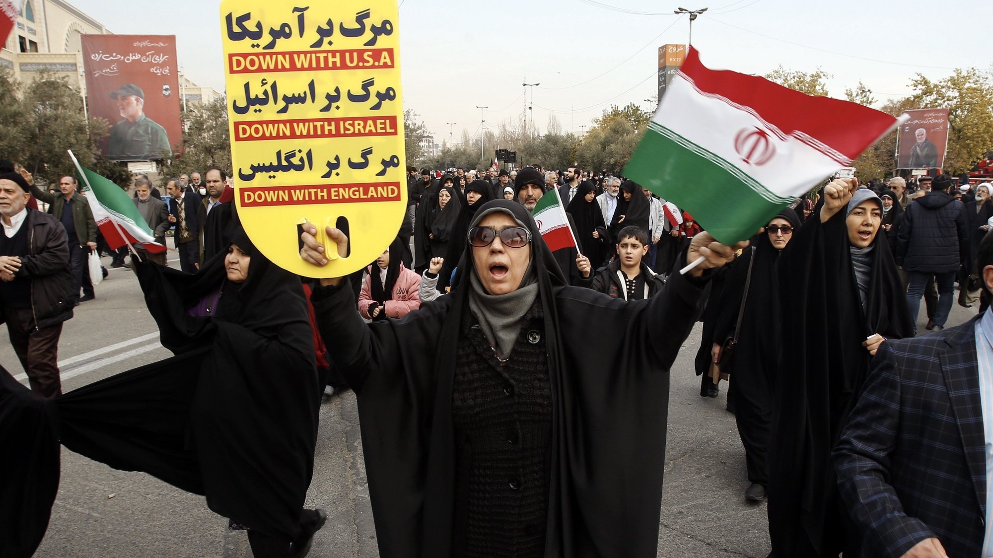 epa11058920 An Iranian woman carrying a placard and an Iranian flag shout slogans during a protest to condemn the recent deadly explosions in the southern city of Kerman, after the Friday prayers in Tehran, Iran, 05 January 2024. On the fourth anniversary of the assassination of Iranian General Qasem Soleimani, two explosions killed more than 70 people and wounded another 171 near the mausoleum dedicated to him, according to Iranian state television. As part of a ceremony to honor General Soleimani, who was killed in a drone strike in neighboring Iraq in 2020, hundreds of people were on their way towards the grave on 03 January.  EPA/ABEDIN TAHERKENAREH