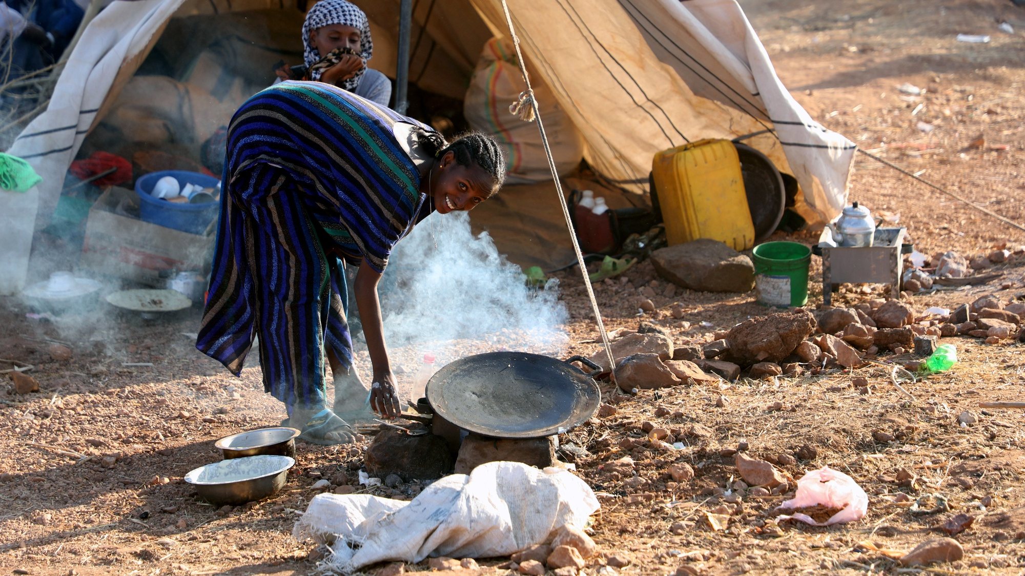 epa08849891 A woman preparing a meal outside her temporary shelter at Um Rakuba refugee camp in the state of al-Qadarif (also known as Gedaref), Sudan, 28 November 2020. The number of refugees in this camp reached nearly 10,000 refugees who crossed the border from Ethiopia to Sudan to escape the conflict in Tigray region of Ethiopia.  EPA/MOHAMMED ABU OBAID