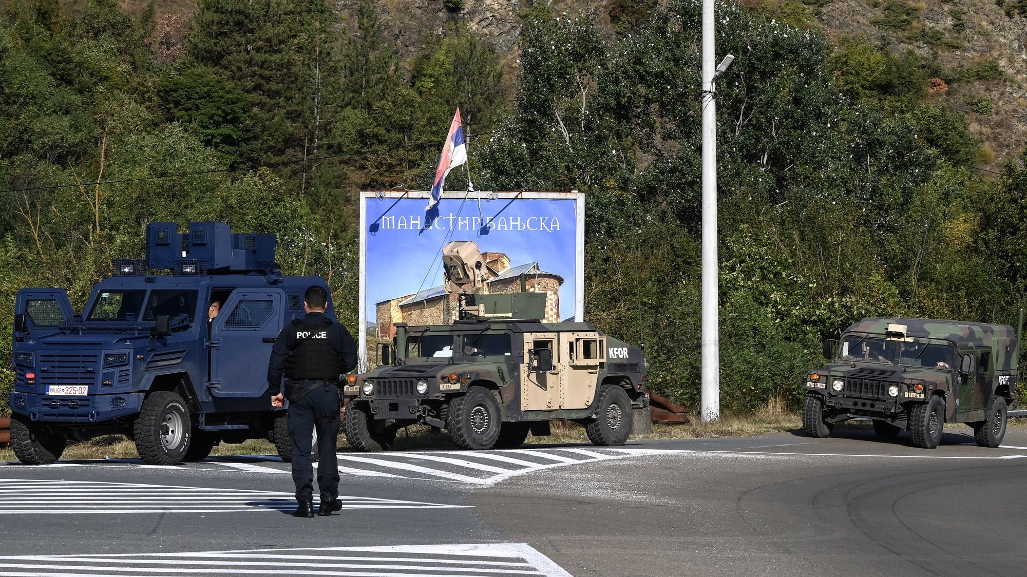 epa10883381 Armed Kosovo police officers secure a road, as Kosovo Force (KFOR) military vehicles are seen in the background, near the village of Banjska, Kosovo, 26 September 2023. A Kosovo Albanian police officer on 24 September was killed by Serb gunmen, who later barricaded themselves in the XIV century Serbian Orthodox Banjska monastery and traded gunfire with Kosovo police for hours. The police regained control of the area late on 24 September. The incident comes at a fragile moment in the Kosovo - Serbia European Union-facilitated dialogue to normalize ties between the two parties.  EPA/GEORGI LICOVSKI