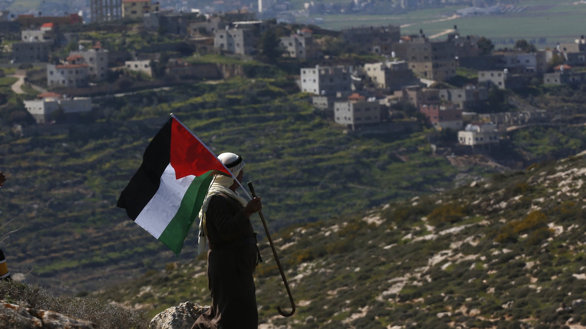 epa09038334 A Palestinian man waves Palestine flag during a demonstration against Israel&#039;s settlements in the village of Bet Dajan near the northern West Bank city of Nablus, 26 February 2021.  EPA/ALAA BADARNEH