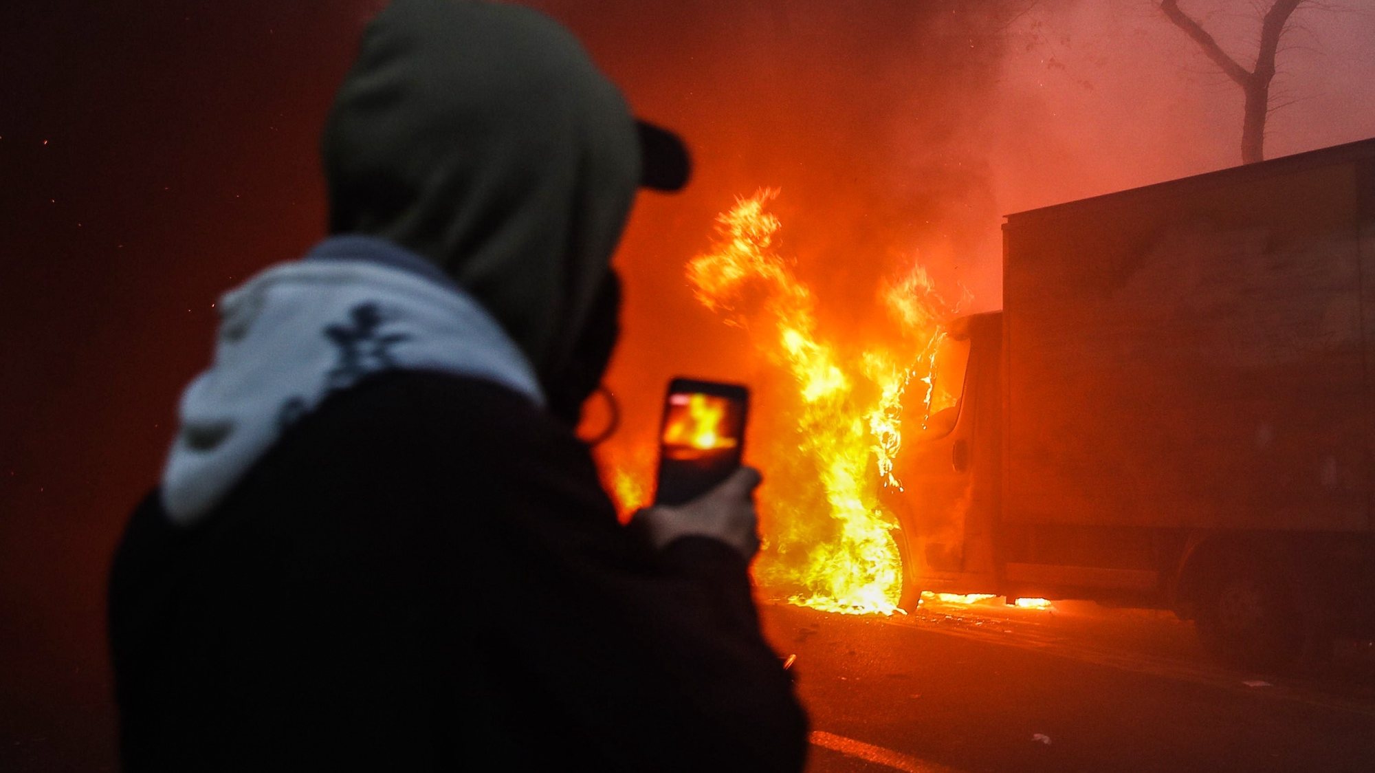 epaselect epa08864958 A man records on his phone a car burning during a protest against France&#039;s controversial global security law, during a protest in a street between Porte des Lilas and Gambetta square, in Paris, France, 05 December 2020. The global security legislation passed by the French Parliament aims to ban the distribution of photos in which police officers and gendarmes can be identified in a way which is harmful to their image  EPA/Mohammed Badra