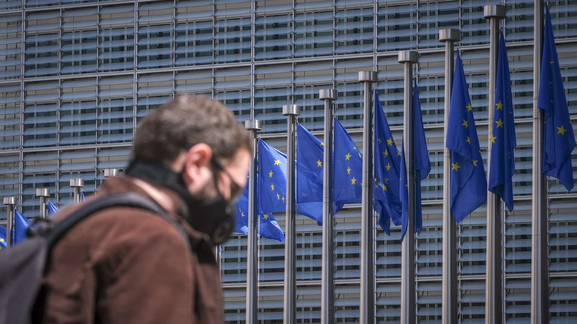 epa08443018 A man wearing a face mask walks in front of the European Commission flags at the Berlaymont building headquarters in Brussels, Belgium, 25 May 2020. Countries around the world are gradually easing COVID-19 lockdown restrictions in an effort to restart the economy and help people in their daily routines.  EPA/OLIVIER HOSLET