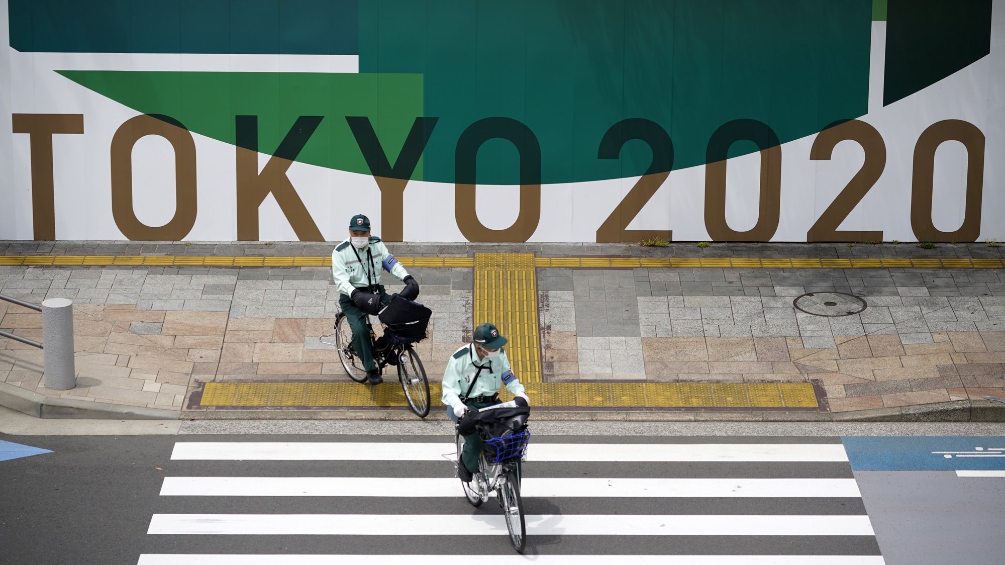epa09196428 Traffic wardens cycle past a Tokyo Olympics advertising board in Tokyo, Japan, 12 May 2021 (issued 13 May 2021). On 13 May 2021, the National Doctors Union requested the government to cancel the Tokyo Olympics, saying that the response to the coronavirus pandemic should be prioritized.  EPA/FRANCK ROBICHON