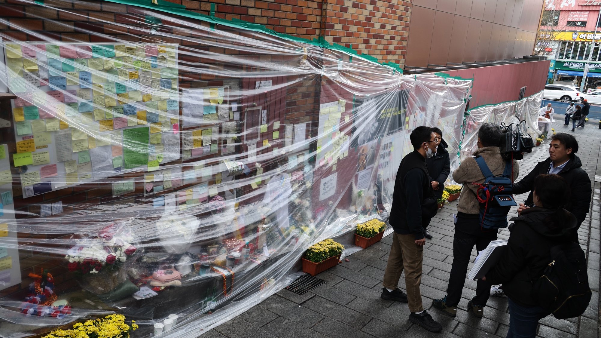epa10333602 Flowers and messages are covered with plastic amid rain at a makeshift memorial space near the site of the Itaewon tragedy in Seoul, South Korea, 28 November 2022. The Halloween crowd crush left 158 people dead.  EPA/YONHAP SOUTH KOREA OUT