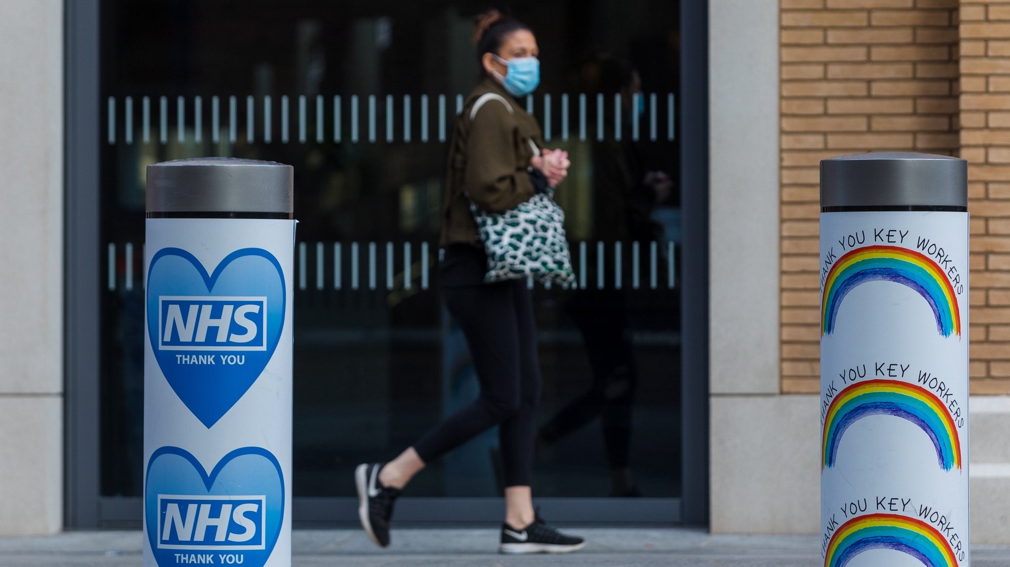 epa08870398 A woman wearing a face mask walks past an NHS bollard near Guy&#039;s Hospital in London, Britain, 08 December 2020. Margaret Keenan, 90, became the first person in the UK to receive the Pfizer-BioNTech Covid-19 vaccine on 08 December and NHS hospitals across Britain will now start to roll out the Pfizer BioNTech Covid-19 vaccine.  EPA/VICKIE FLORES