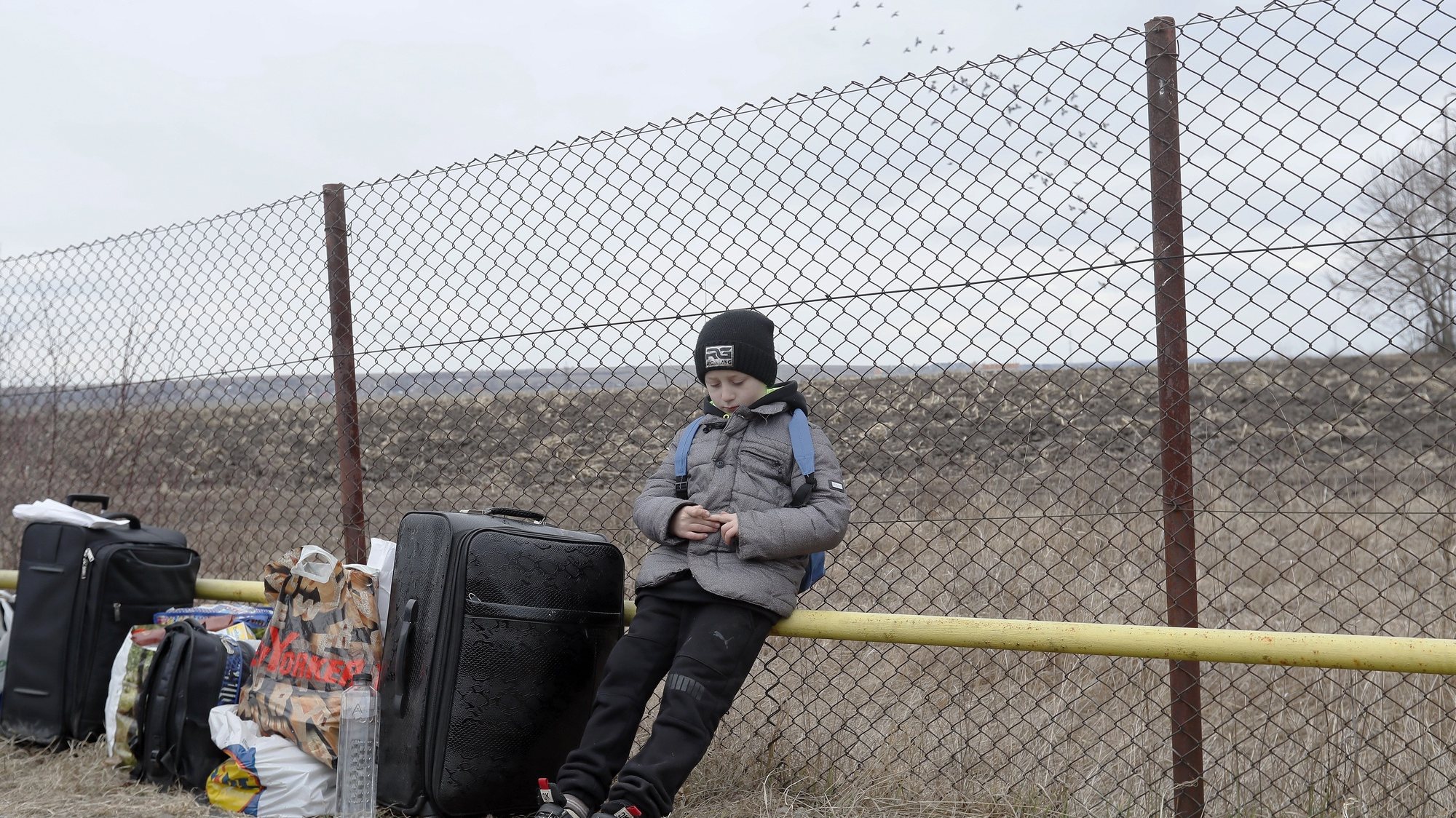 Um rapaz refugiado ucraniano espera pela sua mãe perto das malas da família depois de passarem a fronteira Roménia-Ucrânia em Siret, perto da Roménia. 27 de fevereiro de 2022