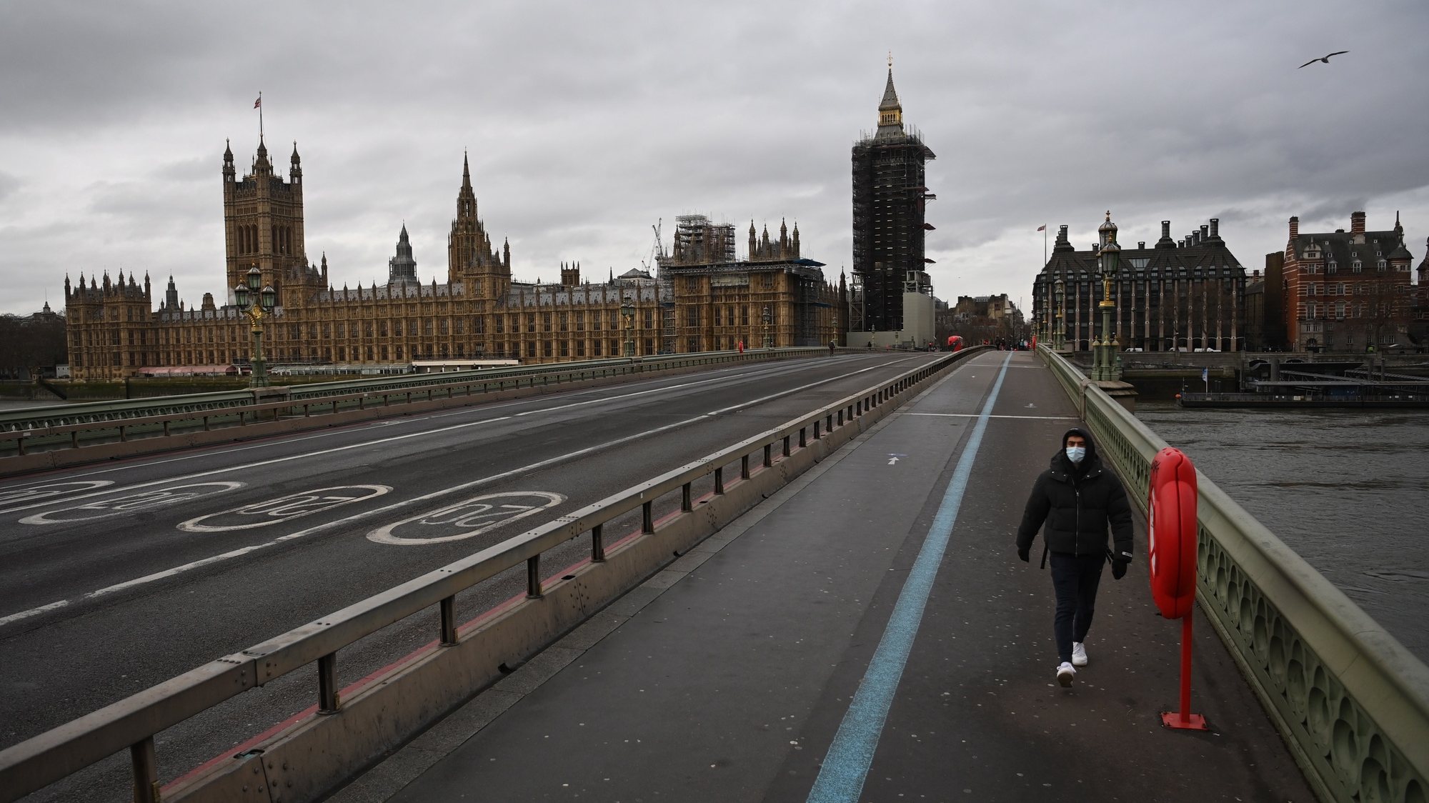 epa08920043 A masked man passes a quiet Westminster Bridge in London, Britain, 05 January 2021.  British Prime Minister Boris Johnson announced on 04 January evening that there would be a third national lockdown in England. The regulations, expected to remain in place until the middle of February, will be presented in parliament on 05 January and subject to a vote on 06 January 2021.  EPA/NEIL HALL