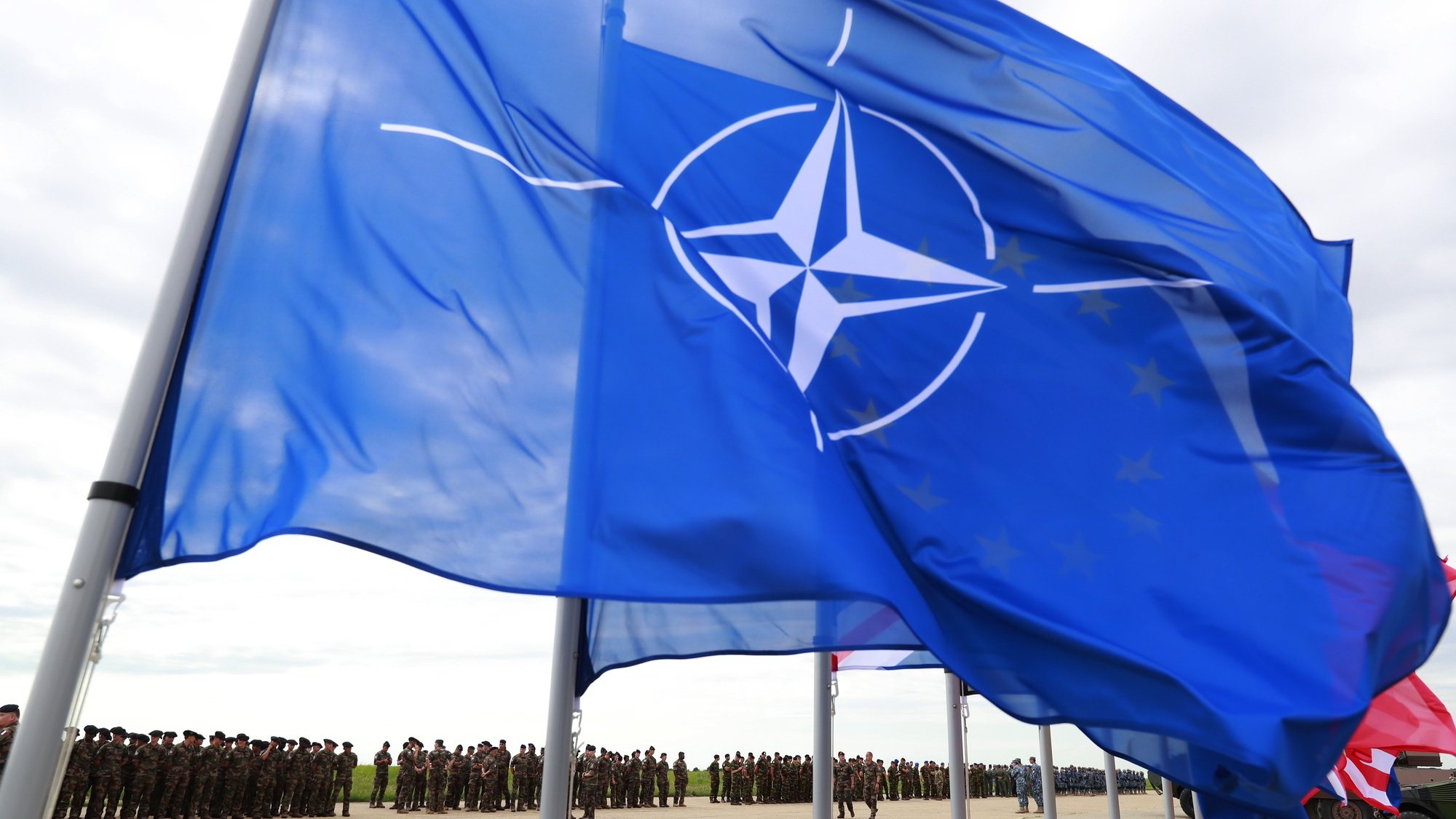 epa10014202 The NATO flag waves in the wind as troops stand in line before being reviewed by French President Macron at Mihail Kogalniceanu Air Base, near the city of Constanta, Romania, 15 June 2022. Macron paid a visit to the military airbase to meet troops stationed in Romania with the NATO Response Force as part of Mission &#039;Aigle&#039; (Eagle). Macron and his Romanian counterpart Iohannis addressed the consolidation of the Romanian-French Strategic Partnership, renewed in 2018 in Paris, by the two presidents who signed a Joint Political Declaration. The two presidents will also approach the support of the Republic of Moldova, which is facing the effects of Russiaâ€™s aggression in Ukraine, by continuing its efforts to assist through the Support Platform for Moldova, created at the initiative of Romania, France and Germany in April 2022.  EPA/ROBERT GHEMENT