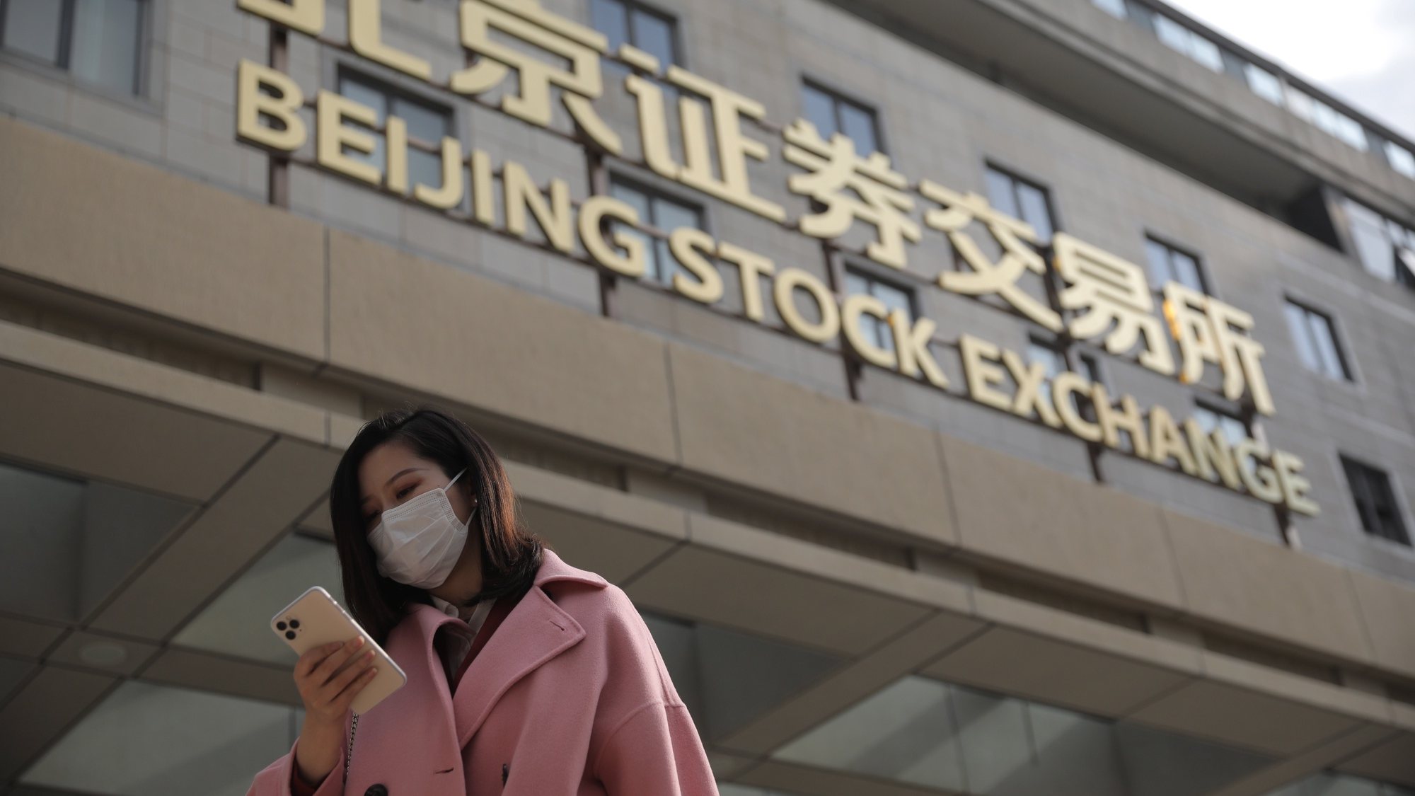 epa09582755 A woman stands outside the new Beijing Stock Exchange building at the Financial Street in Beijing, China, 15 November 2021. The Beijing Stock Exchange opens on 15 November, with the aim of nurturing more technologically advanced small and medium-sized enterprises.  EPA/WU HONG