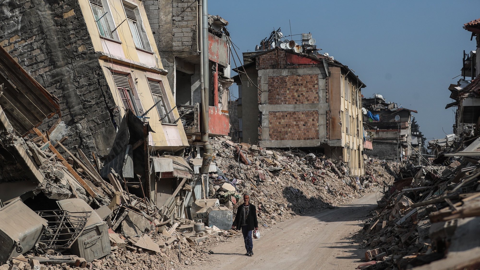 epa10485023 A man walks past collapsed buildings in the aftermath of powerful earthquakes in Hatay, Turkey, 23 February 2023. More than 46,000 people died and thousands more were injured after major earthquakes struck southern Turkey and northern Syria on 06 February and again on 20 February.  EPA/ERDEM SAHIN