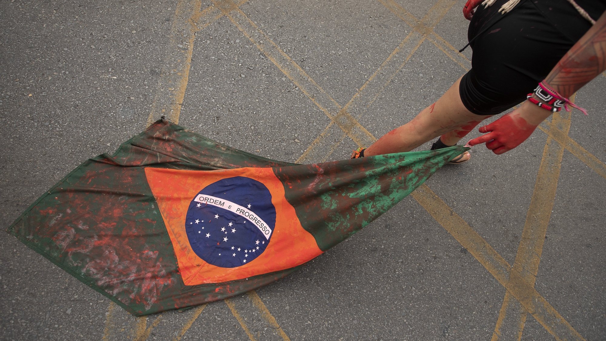 epa09885189 An indigenous woman, belonging to one of the peoples gathered at the Free Land Camp (ATL), protests by dragging a Brazilian flag symbolically covered in blood during an act called &#039;Ouro de Sangue&#039; (Gold of Blood), against the increase in mining in indigenous territories, in Brasilia, Brazil, 11 April 2022. The ATL takes place at a time when the National Congress and the Federal Government are voting on projects that violate the rights of indigenous peoples, such as Bill 191/2020.  EPA/Joedson Alves