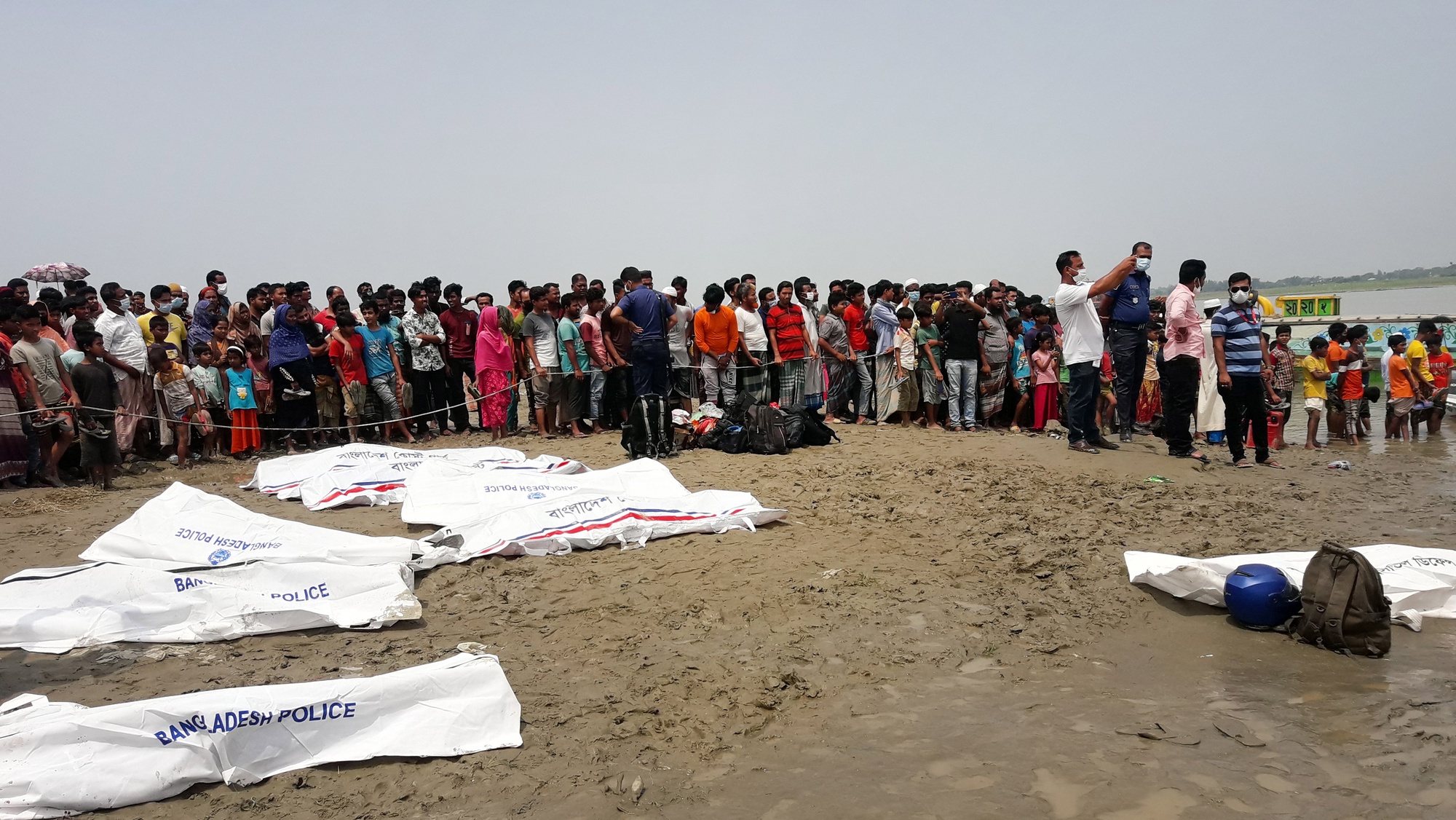epa09175113 Local people stand by the river as they look at rescue workers lay out the bodies recovered from the river in body bags after a speedboat collided with another boat in the Padma River in Madaripur District,  Bangladesh, 03 May 2021. Local police said at least 26 people were killed and several others went missing after the incident.  EPA/STR