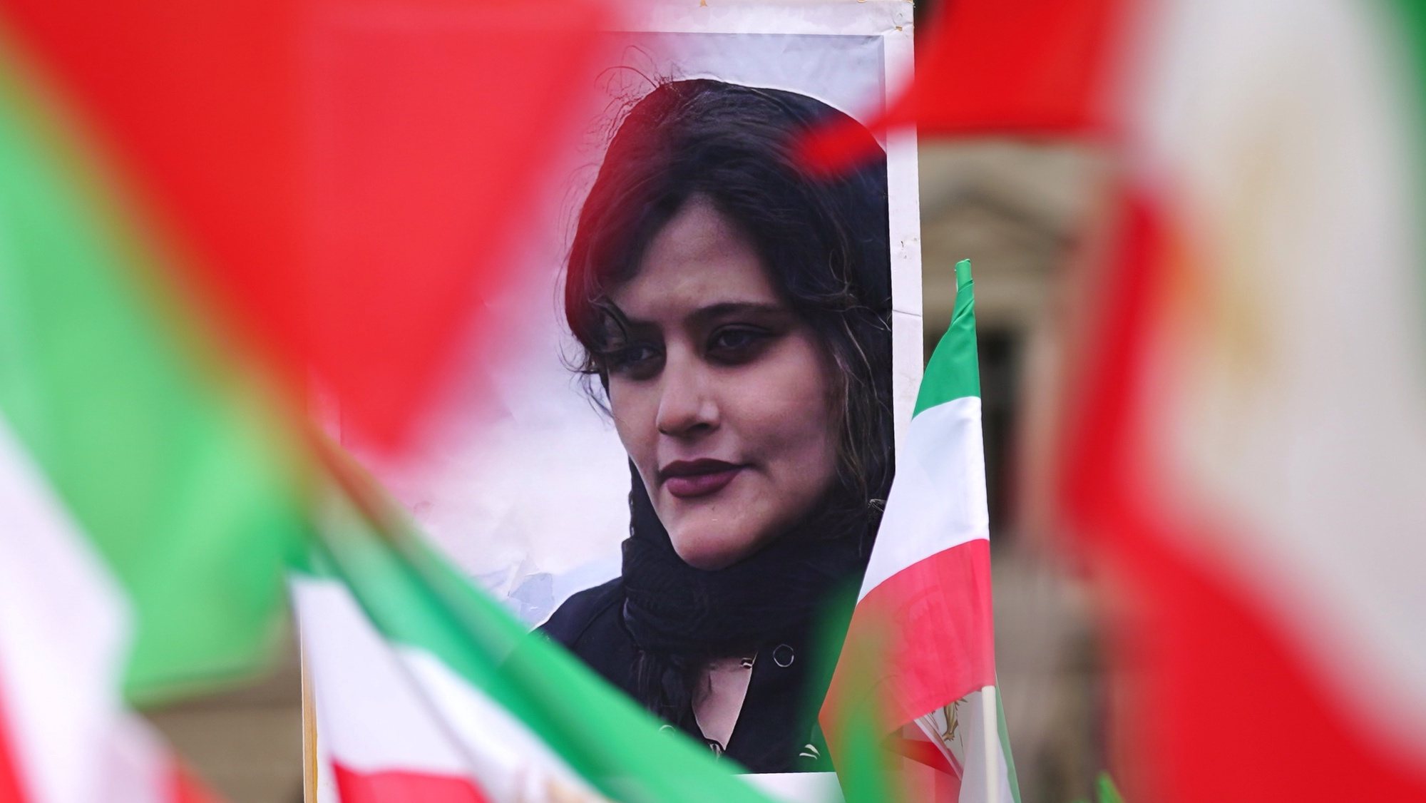 epa10217479 A portrait of Mahsa Amini stands between Iranian national flags during a &#039;Solidarity with the civil uprising in Iran&#039; rally at Bebel Platz square in Berlin, Germany, 01 October 2022. Protests have erupted in Iran and across the world after the death of Mahsa Amini who died in the custody of Iran&#039;s morality police.  EPA/CLEMENS BILAN
