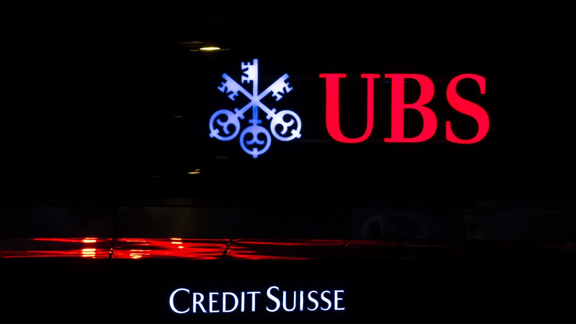 epa10529298 The illuminated logos of the Swiss banks Credit Suisse and UBS are displayed on buildings in Zurich, Switzerland, 18 March 2023. Shares of Credit Suisse lost more than one-quarter of their value on 15 March, hitting a record low after its biggest shareholder, the Saudi National Bank, told outlets that it would not inject more money into the ailing Swiss bank.  EPA/MICHAEL BUHOLZER