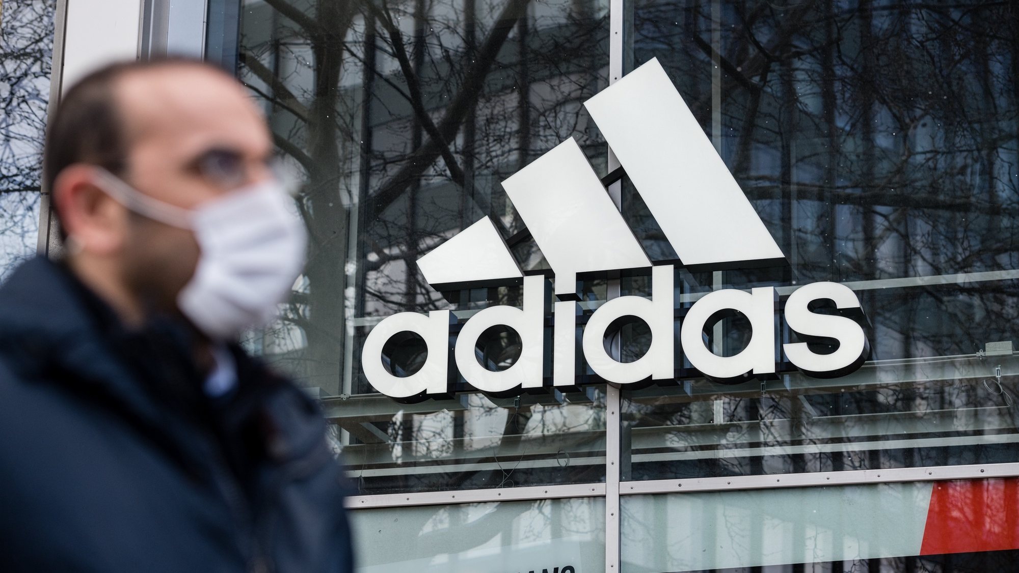 epa08334148 A man with protective mask in front of adidas store with the logo of the sporting goods manufacturer, in Berlin, Germany, 31 March 2020. The German government and local authorities are heightening measures to stem the spread of the coronavirus SARS-CoV-2 which causes the Covid-19 disease.  EPA/JENS SCHLUETER