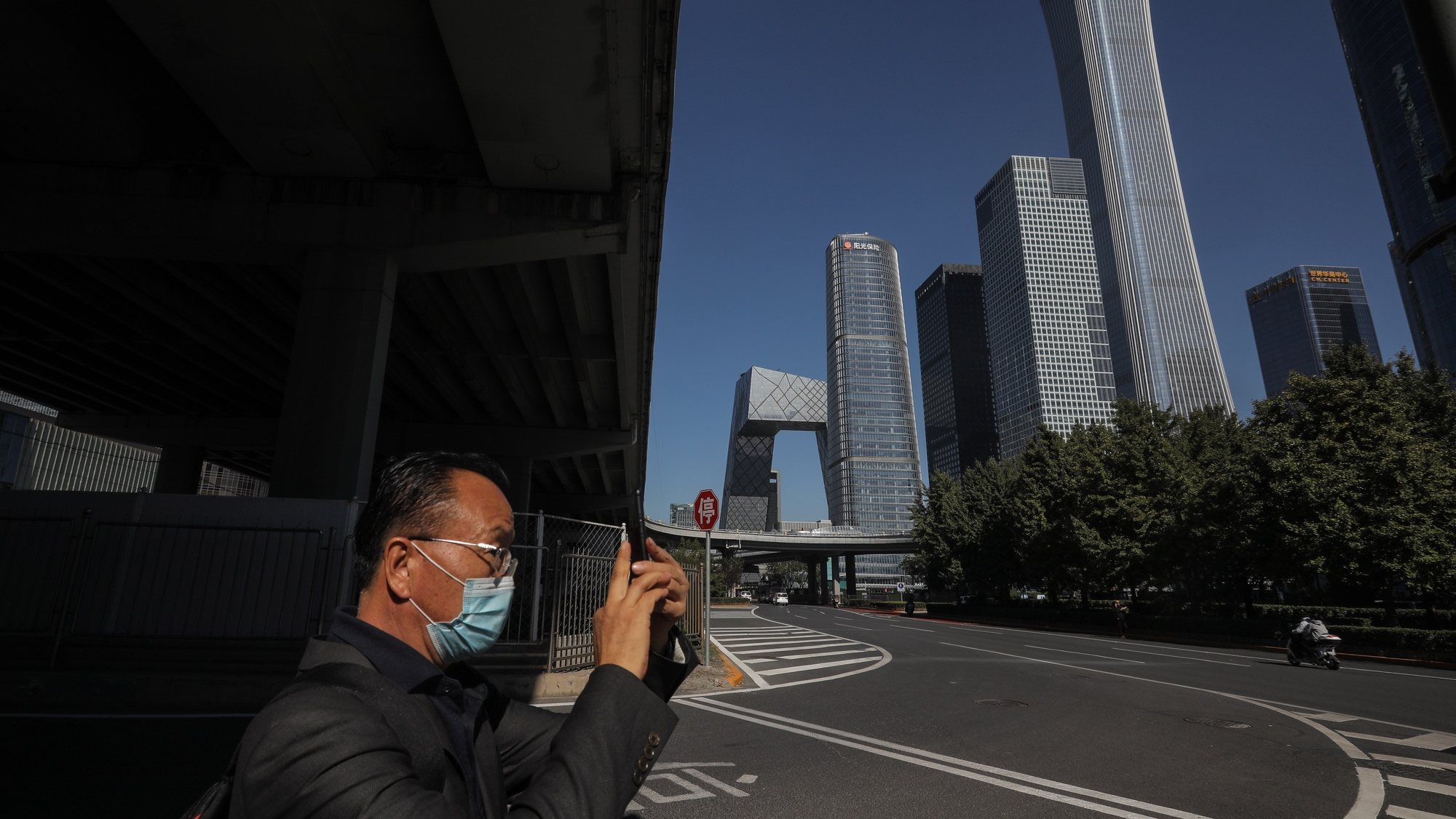 epa09529478 A man uses his mobile phone to take photos in the central business district (CBD) in Beijing, China, 17 October 2021 (issued 18 October 2021). China&#039;s gross domestic product (GDP) rose 4.9 percent year on year in the third quarter of 2021, according to data from the National Bureau of Statistics (NBS) issued on 18 October 2021.  EPA/WU HONG