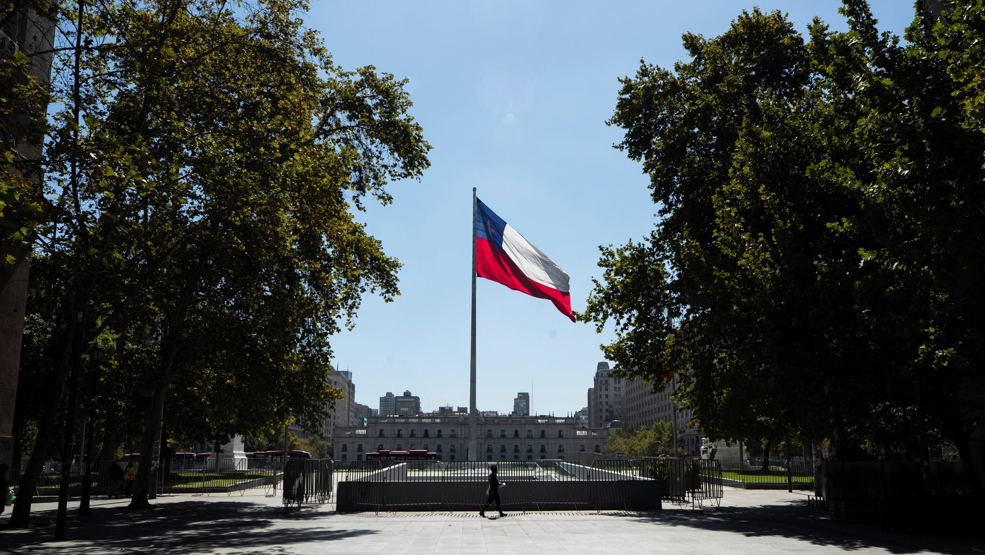 epa09100158 A man passes in front a Chile&#039;s national flag prior the start of a quarantine period to slow the spread of the coronavirus, at a square in front of la Moneda Presidential Palace in Santiago, Chile, 26 March 2021.  EPA/Alberto Valdes
