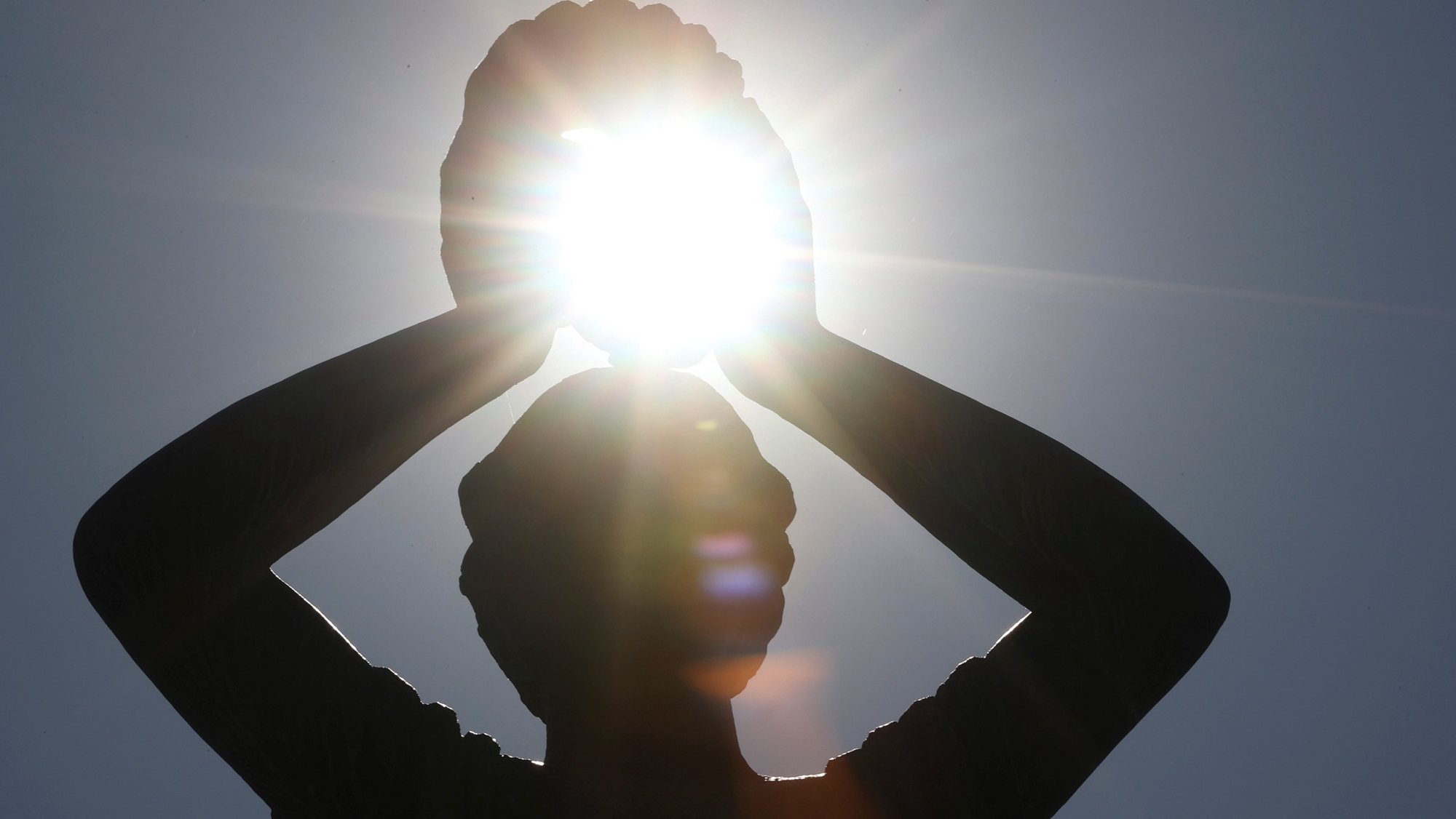 epa08578479 The sun is seen between the hands of a sculpture at Retiro Park in Madrid, Spain, 01 August 2020, during the heat wave that brought temperatures of over 40 degrees Celsius.  EPA/Mariscal