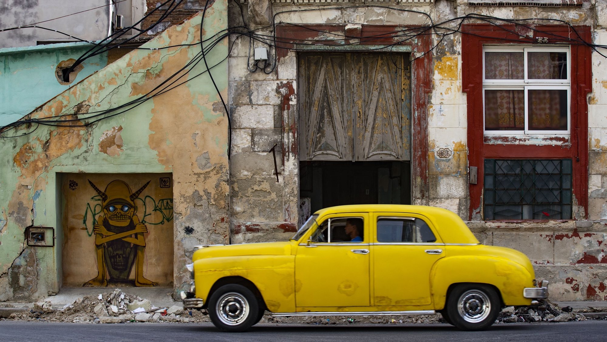 epa11057110 An old automobile in front of a run-down building in Havana, Cuba, 04 January 2024. Cuba is well known for oldtimer cars.  EPA/Yander Zamora