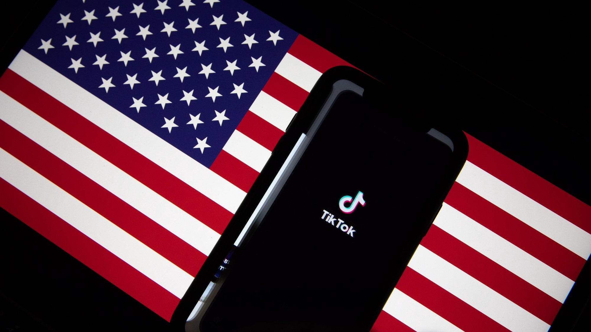 epa08685859 A generic illustration shows the logo of Chinese internet media app TikTok on a phone, and the US flag on a laptop screen, in Beijing, China, 21 September 2020. Chinese-owned mobile app WeChat was set to stop operation in the U.S. on midnight 20 September 2020.  EPA/ROMAN PILIPEY