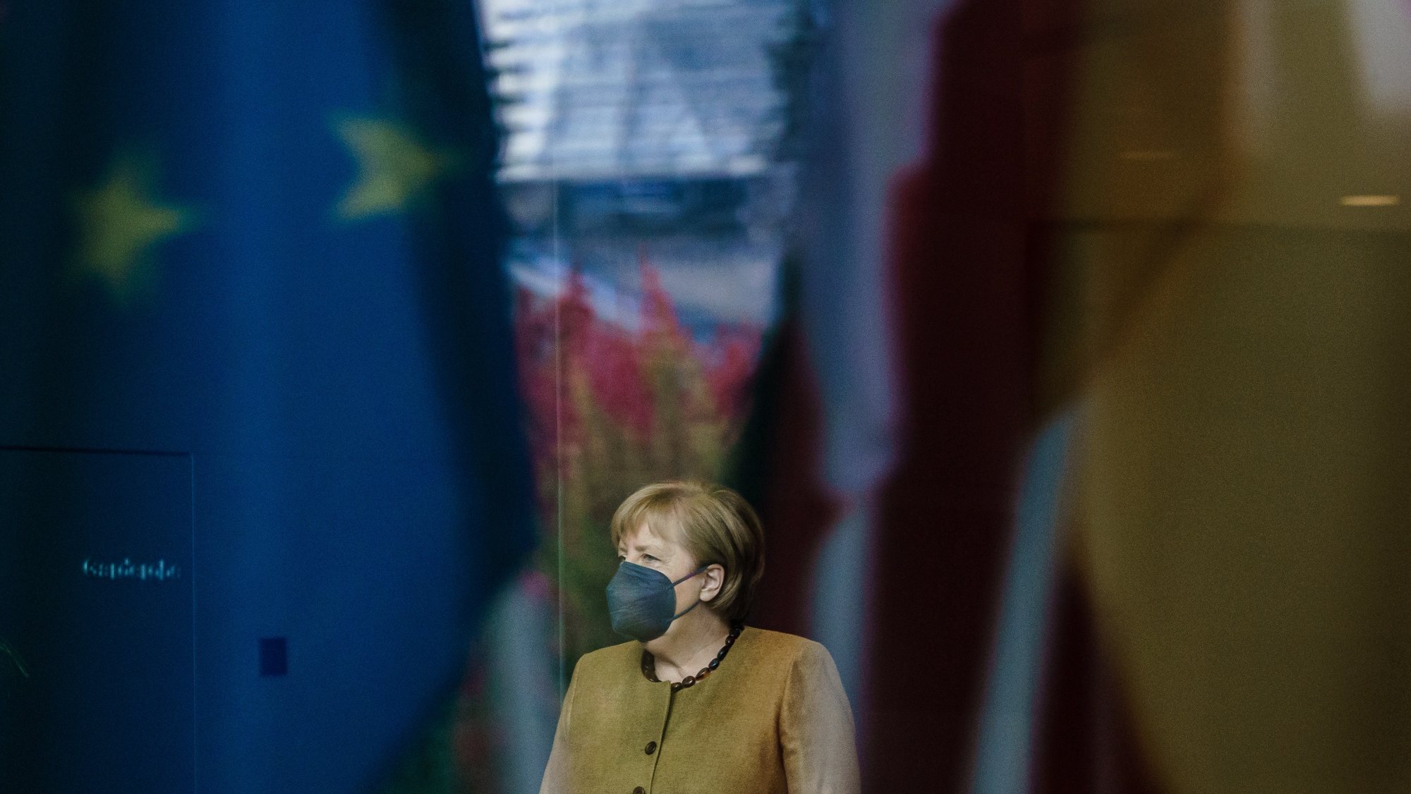 epa09519736 German Chancellor Angela Merkel, seen behind reflections of flags and the dome of the German Parliament &#039;Bundestag&#039;, waits for the arrival of Italian President Sergio Mattarella at the chancellery in Berlin, Germany, 12 October 2021. Merkel and Mattarella meet for bilateral talks. The Italian president is on an official visit to Berlin.  EPA/CLEMENS BILAN