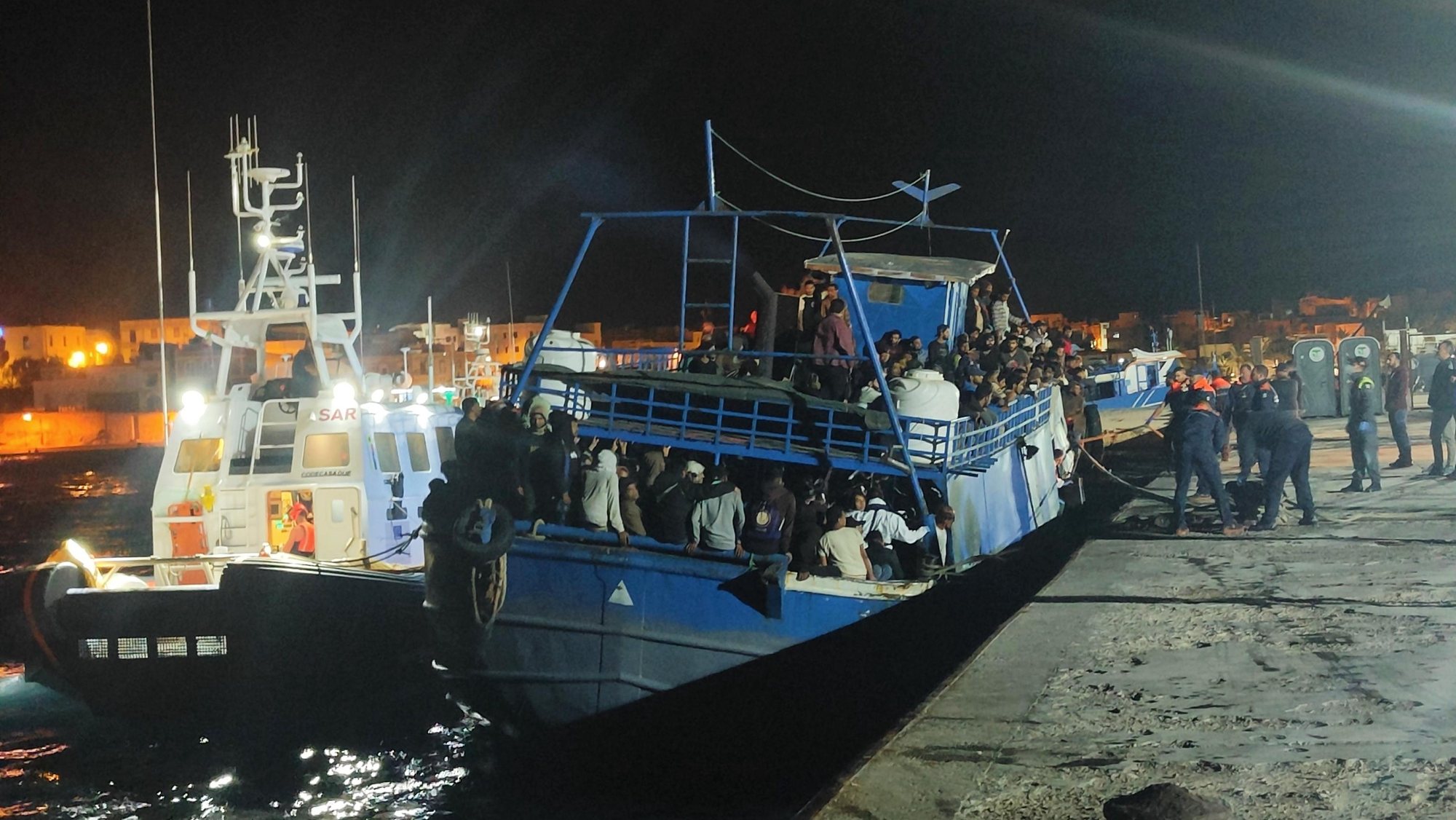 epa10958720 A fishing boat carrying around 400 migrants on board arrived on Lampedusa island and docked at the commercial pier where disembarkation operations are underway, in Lampedusa, southern Italy, 04 November 2023. A Coast Guard patrol boat escorted the fishing boat to the dock to avoid risks because of strong winds.  EPA/ELIO DESIDERIO