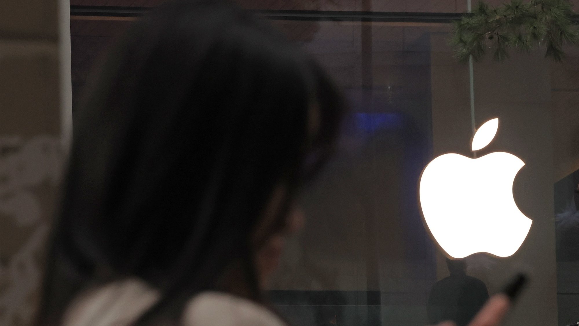 epa11013071 A person uses a mobile phone near an Apple Inc. logo at the Apple Store in Seoul's Myeongdong area, South Korea 06 December 2023. The Seoul High Court ordered Apple the same day to pay 70,000 won (53.30 dollars) in compensation to each of seven South Korean iPhone users for intentionally slowing the performance of their devices after software updates.  EPA/YONHAP