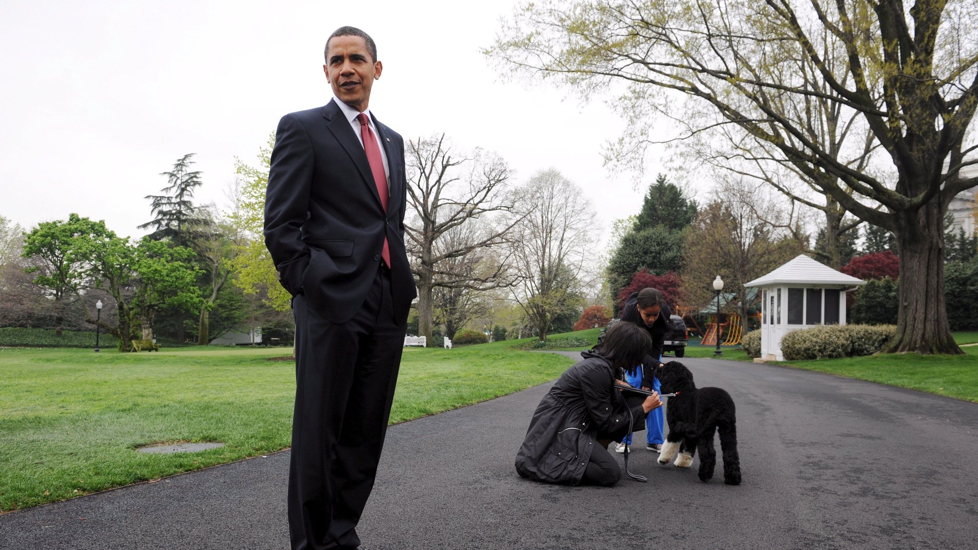 epa09186447 (FILE) - US President Barack Obama (L), speaks to members of the press while First Lady Michelle Obama (back L) and one of their daughters Malia (back R) play with the new White House dog Bo, a six-month-old black-and-white Portuguese water dog, at the South Lawn of the White House in Washington, DC, USA, 14 April 2009 (Reissued 08 May 2021). Former US President Barack Obama and First Lady Michelle Obama announced on 08 May that their dog Bo has died of cancer.  EPA/MICHAEL REYNOLDS