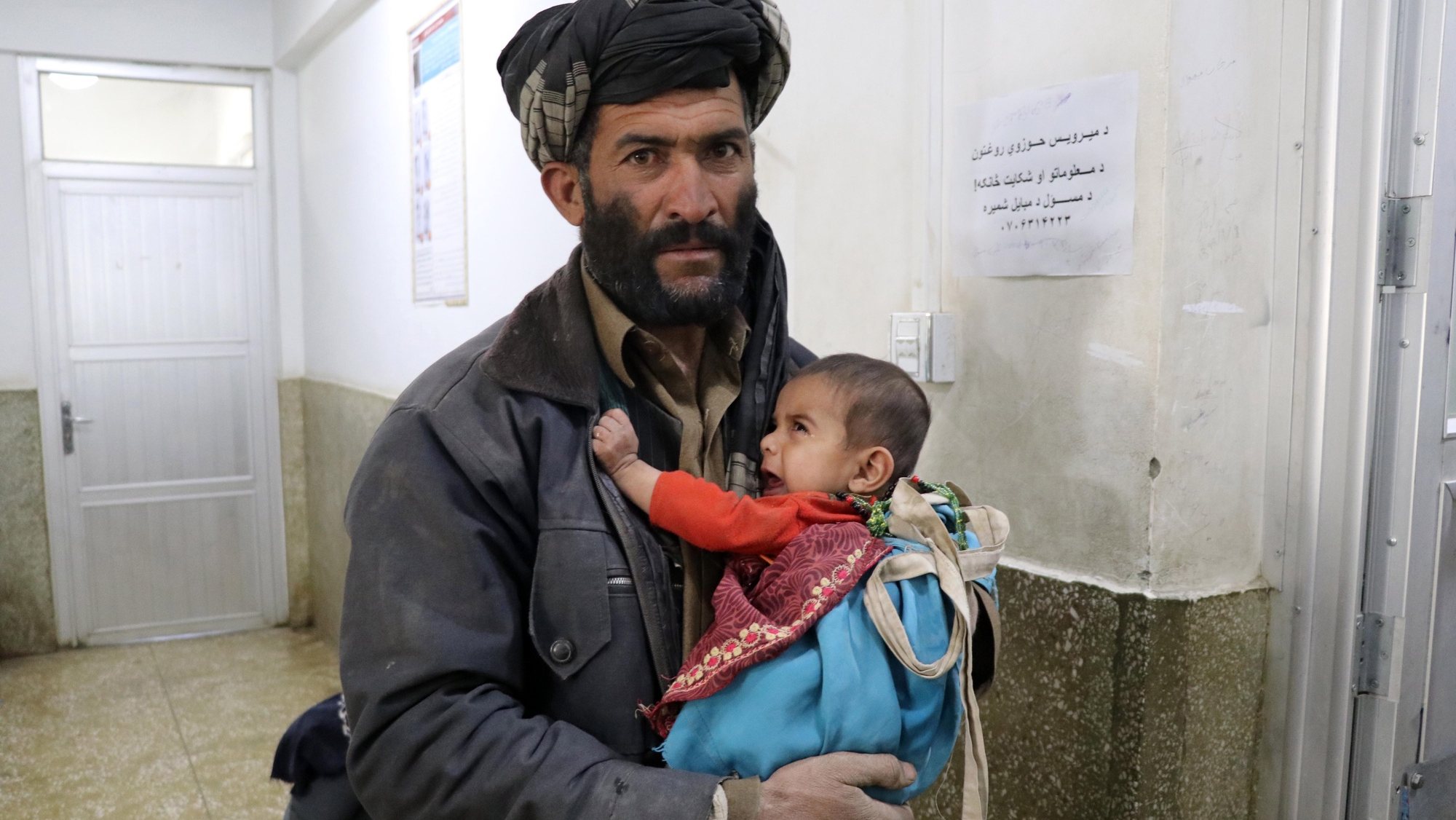 Homem afegão com criança ao colo para receber tratamento num hospital em Kandahar