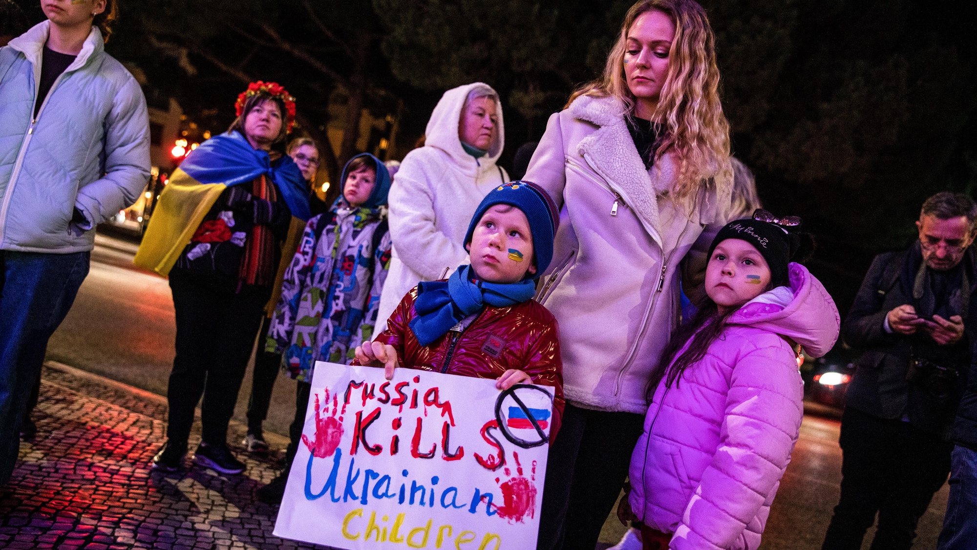 Uma crianças segura um cartaz com a frase “Russia Kills Ucraninian Children” durante uma vigília de um ano de guerra na Ucrânia, promovida pelo Núcleo da Associação dos Ucranianos em Portugal de Leiria, junto ao edifício da Câmara Municipal, 24 de fevereiro de 2023. Na ocasião é cantado o hino nacional da Ucrânia e é feito um minuto de silêncio em memória das vítimas. PAULO CUNHA/LUSA