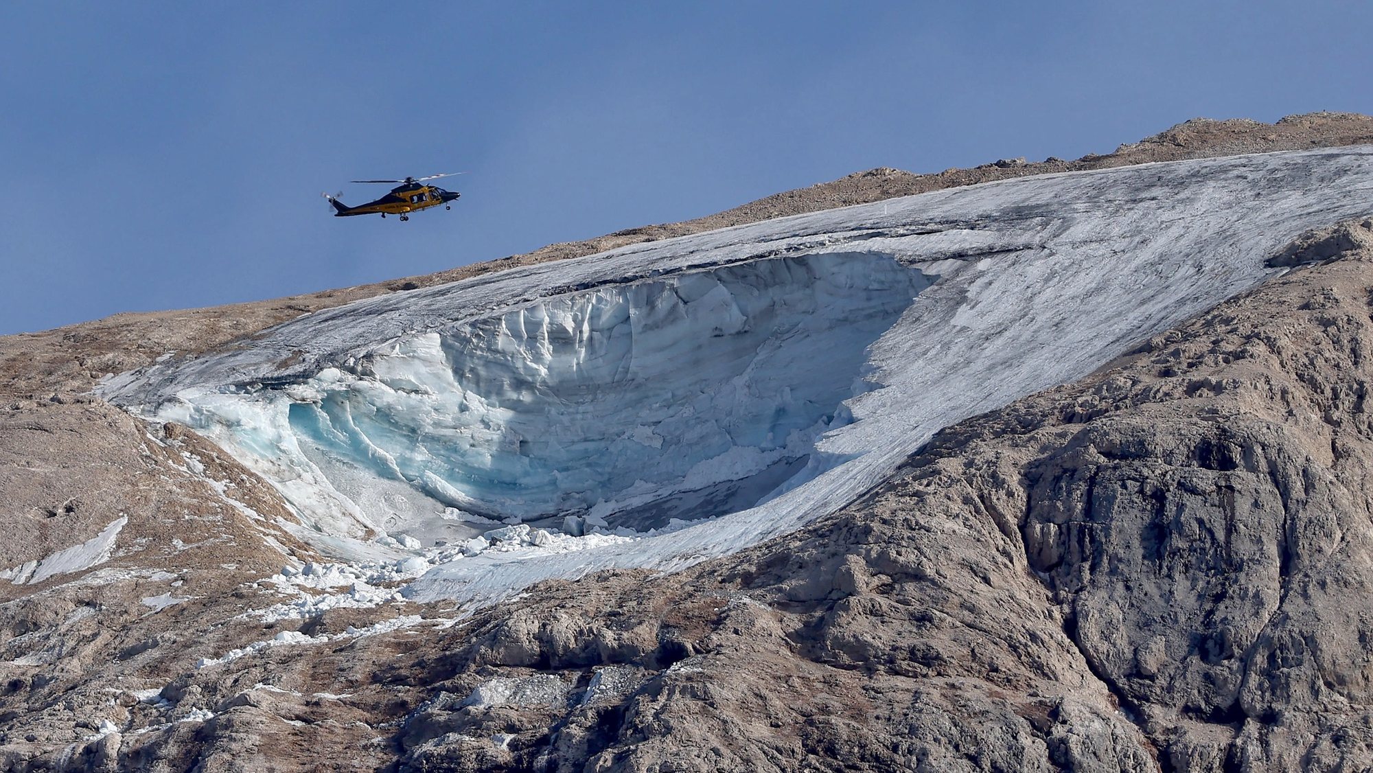 epa10052089 A helicopter flies over the avalanche area in the aftermath of an avalanche on the Marmolada Mountain in Canazei, Italy, 04 July 2022. At least seven people were killed and more than a dozen were still missing on 04 July, a day after a glacier collapsed triggering an avalanche on the multi-peak mountain of the Italian Dolomites. The temperature on the glacier on 03 July was measured at a record 10 degrees Celsius.  EPA/ANDREA SOLERO