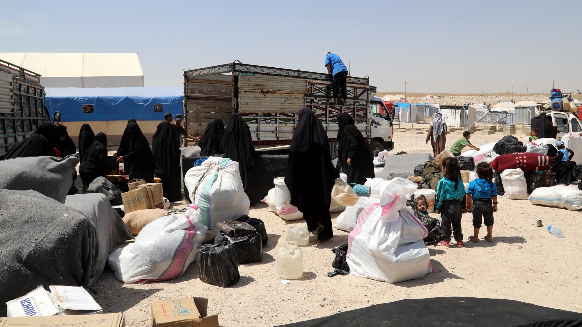 epa07623494 Wives of Islamic state fighters (IS) load their belongings into a truck upon their deportation from the al-Hol camp for refugees in al-Hasakah governorate in northeastern Syria on 03 June 2019 (issued 04 June 2019).  According to media reports, the Kurdish authorities in northeast Syria are handing over 800 women and children all of them Syrian, including relatives of Islamic state fighters, to their families in the first such transfer from an overcrowded camp.  EPA/AHMED MARDNLI