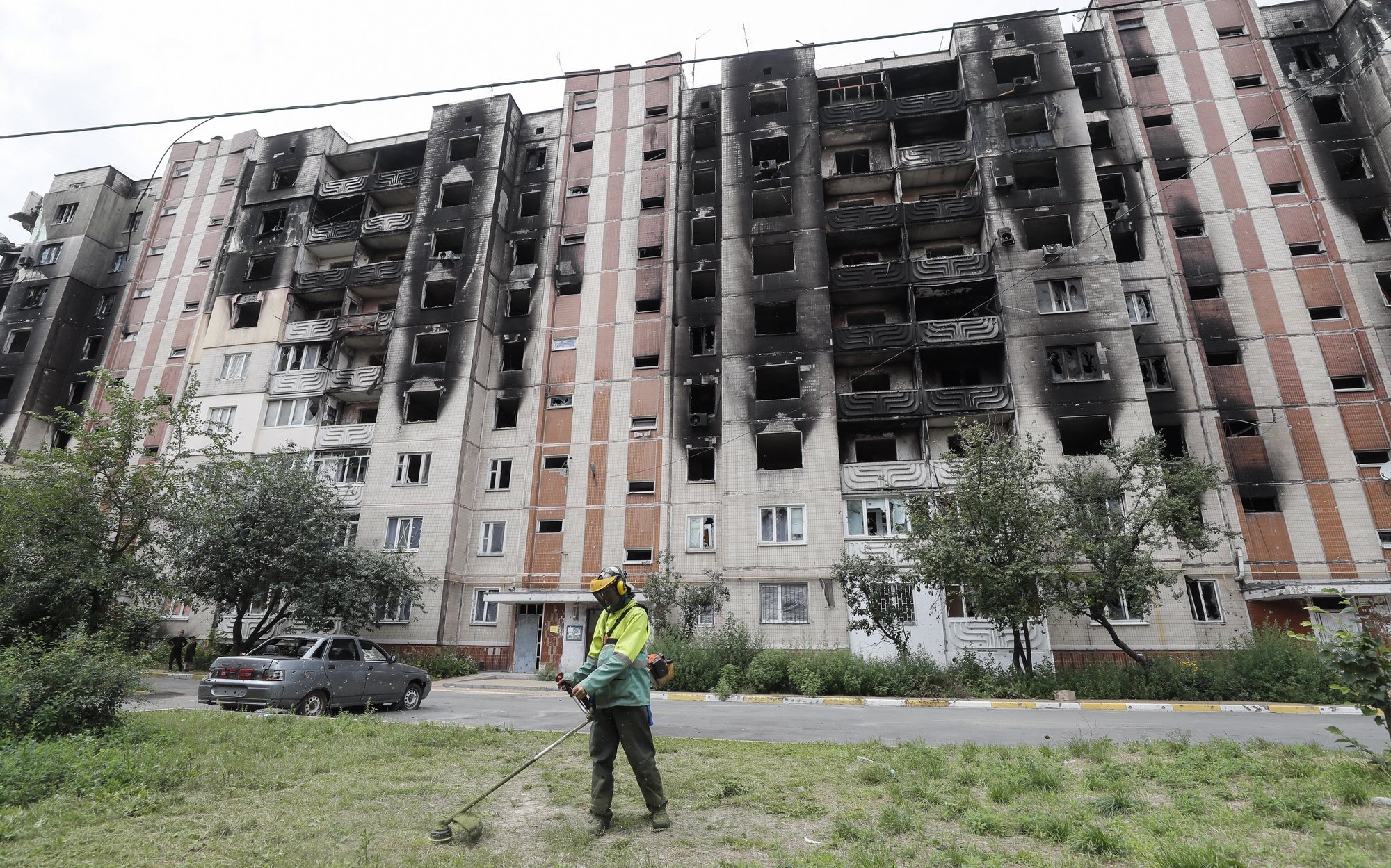 epa10112752 A communal worker mows the grass in front of a damaged residential building in the city of Irpin, near Kyiv, Ukraine, 09 August 2022 as life goes on amid Russia&#039;s military invasion of the country. Irpin as well as other towns and villages in the northern part of the Kyiv region became battlefields and were heavily shelled when Russian troops tried to reach the Ukrainian capital Kyiv in February and March 2022. Russian troops on 24 February entered Ukrainian territory, starting a conflict that has provoked destruction and a humanitarian crisis.  EPA/SERGEY DOLZHENKO