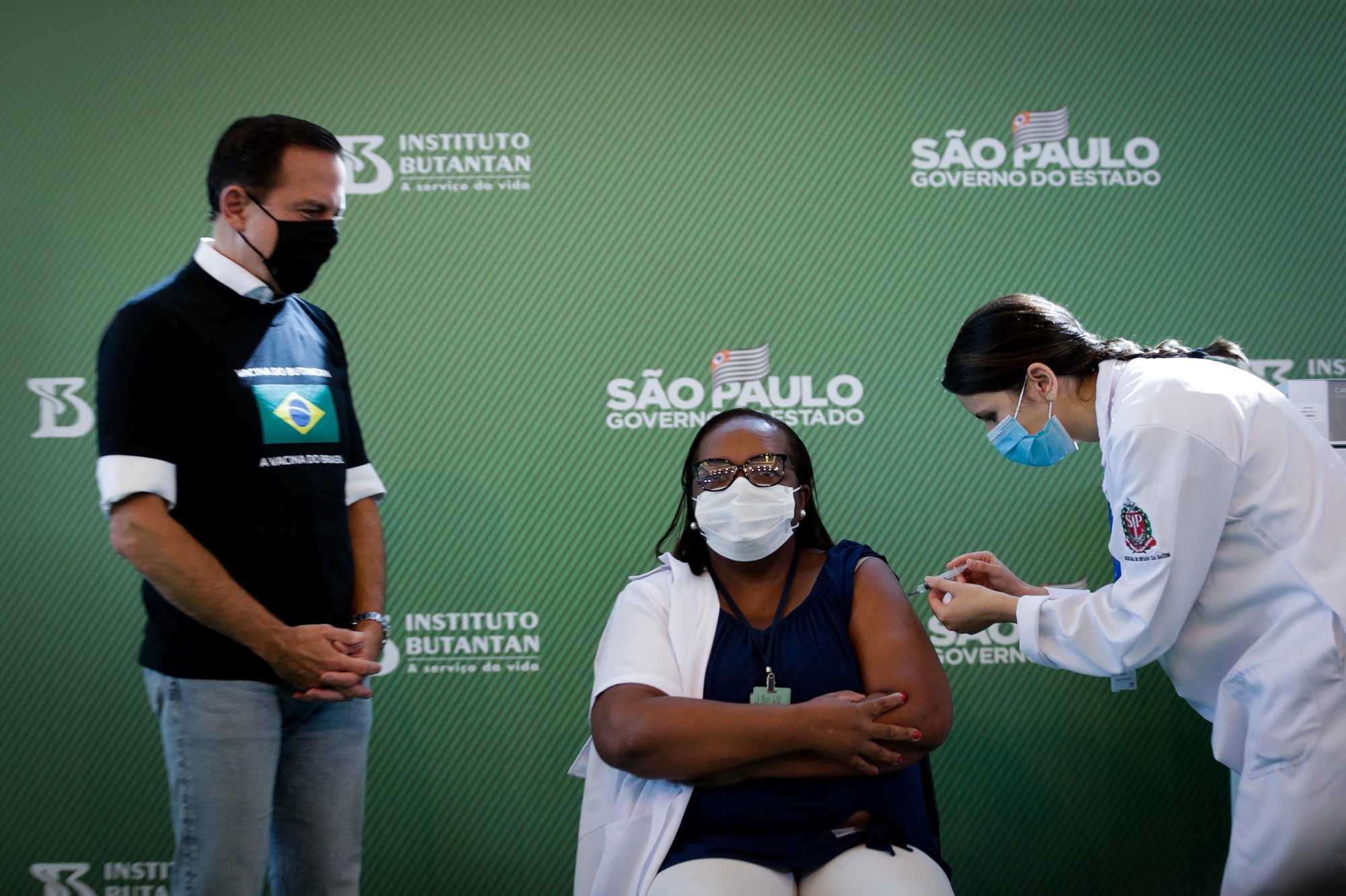 epa08944696 Monica Calazans (C), a nurse at Hospital las Clinicas in the capital of Sao Paulo, receives the vaccine against covid-19 in the presence of the governor of the state of Sao Paulo, Joao Doria (L), in Sao Paulo, Brazil, 17 January 2021. Brazil, one of the countries in the world most affected by the coronavirus pandemic, applied the first dose of the covid-19 vaccine to the 54-year-old nurse this Sunday in Sao Paulo, at a time when the Latin American giant faces a second wave of the disease. The first dose of the vaccine developed by the Chinese laboratory Sinovac and the Brazilian Butantan Institute was administered just minutes after the approval of its emergency use by the National Health Surveillance Agency (Anvisa).  EPA/Fernando Bizerra Jr
