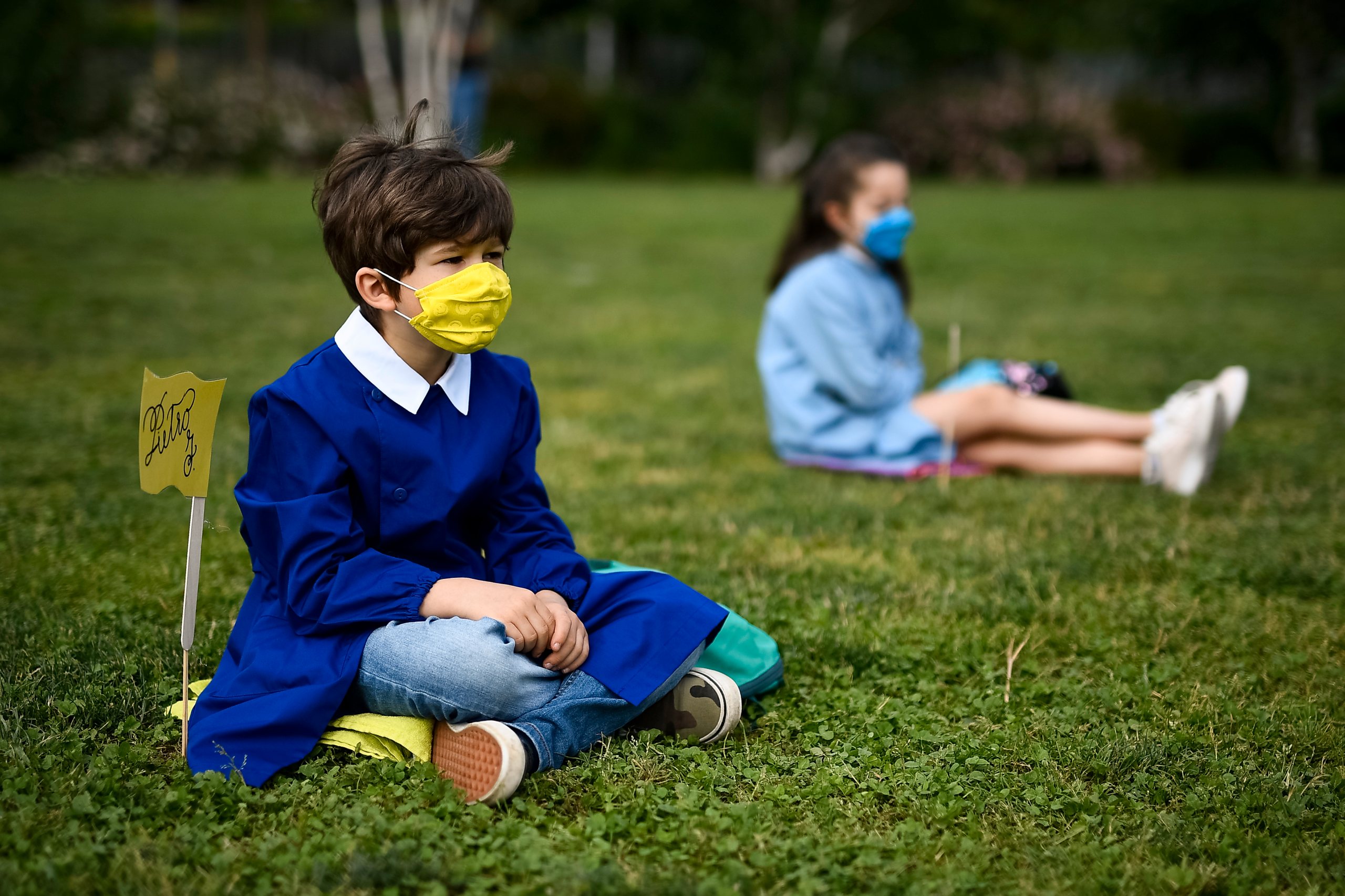 Pupils wearing masks are sitting on the ground during the &#039;