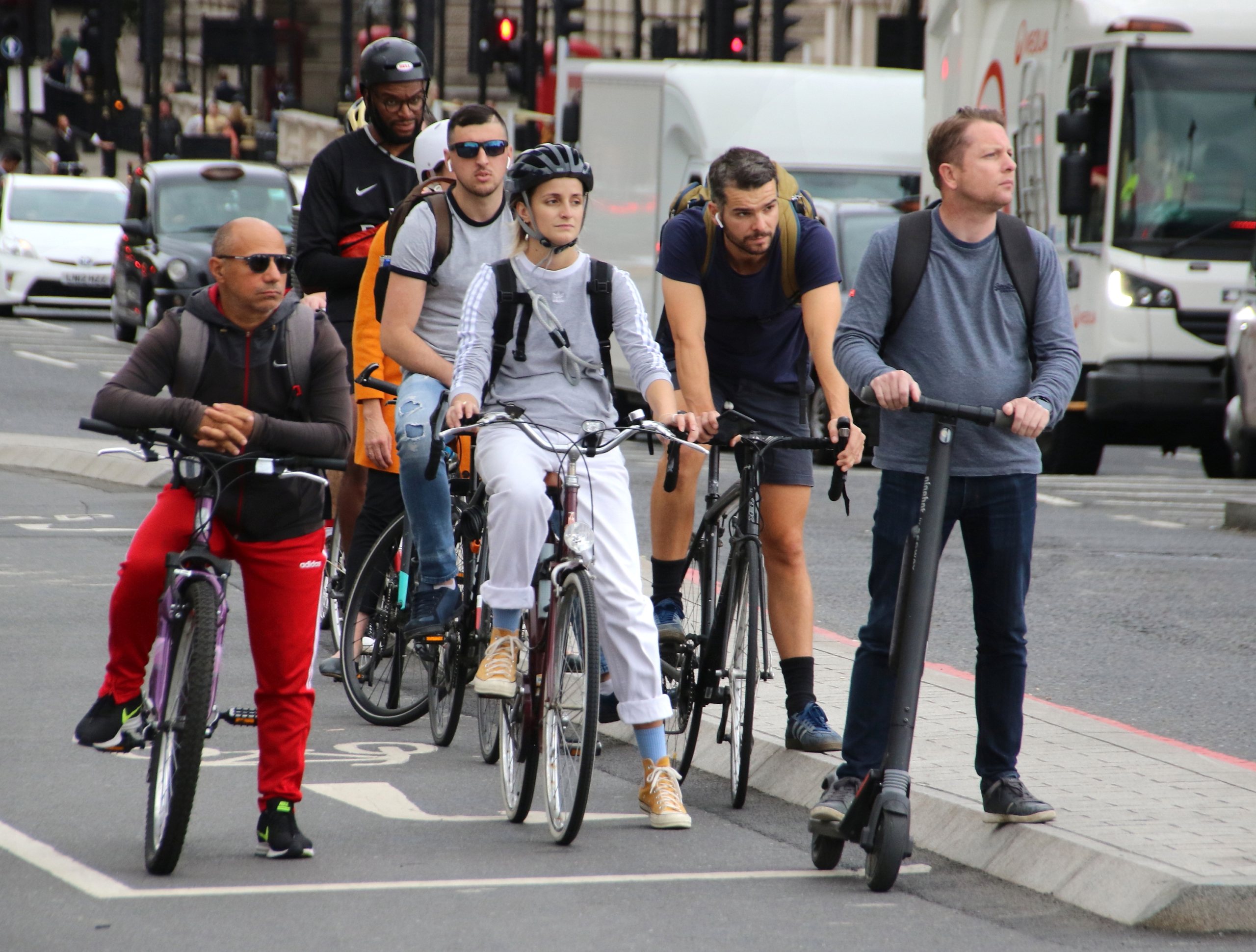 Cyclists and an electric scooter rider wait at traffic