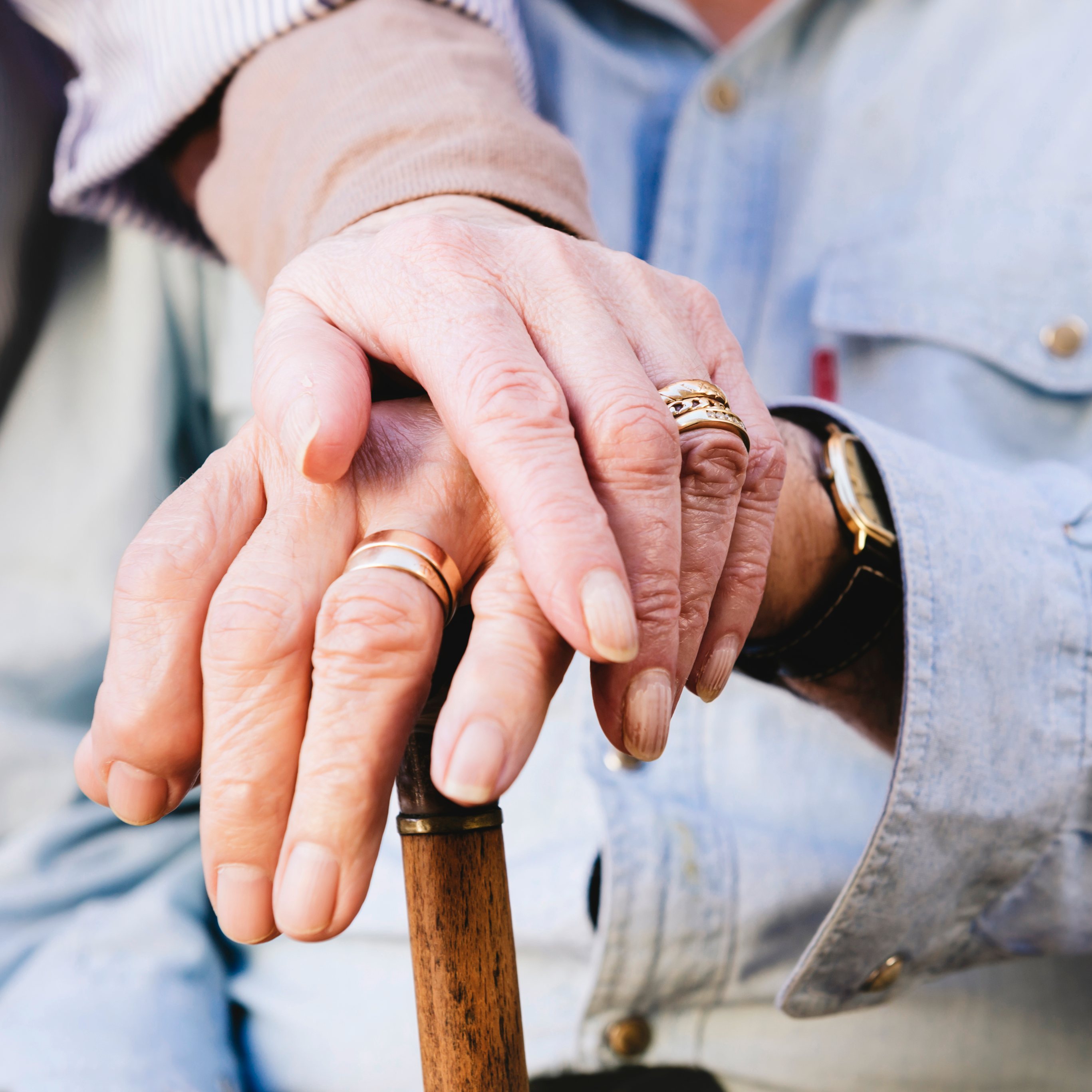 Close-up of old man&#039;s and woman&#039;s hands resting on a cane