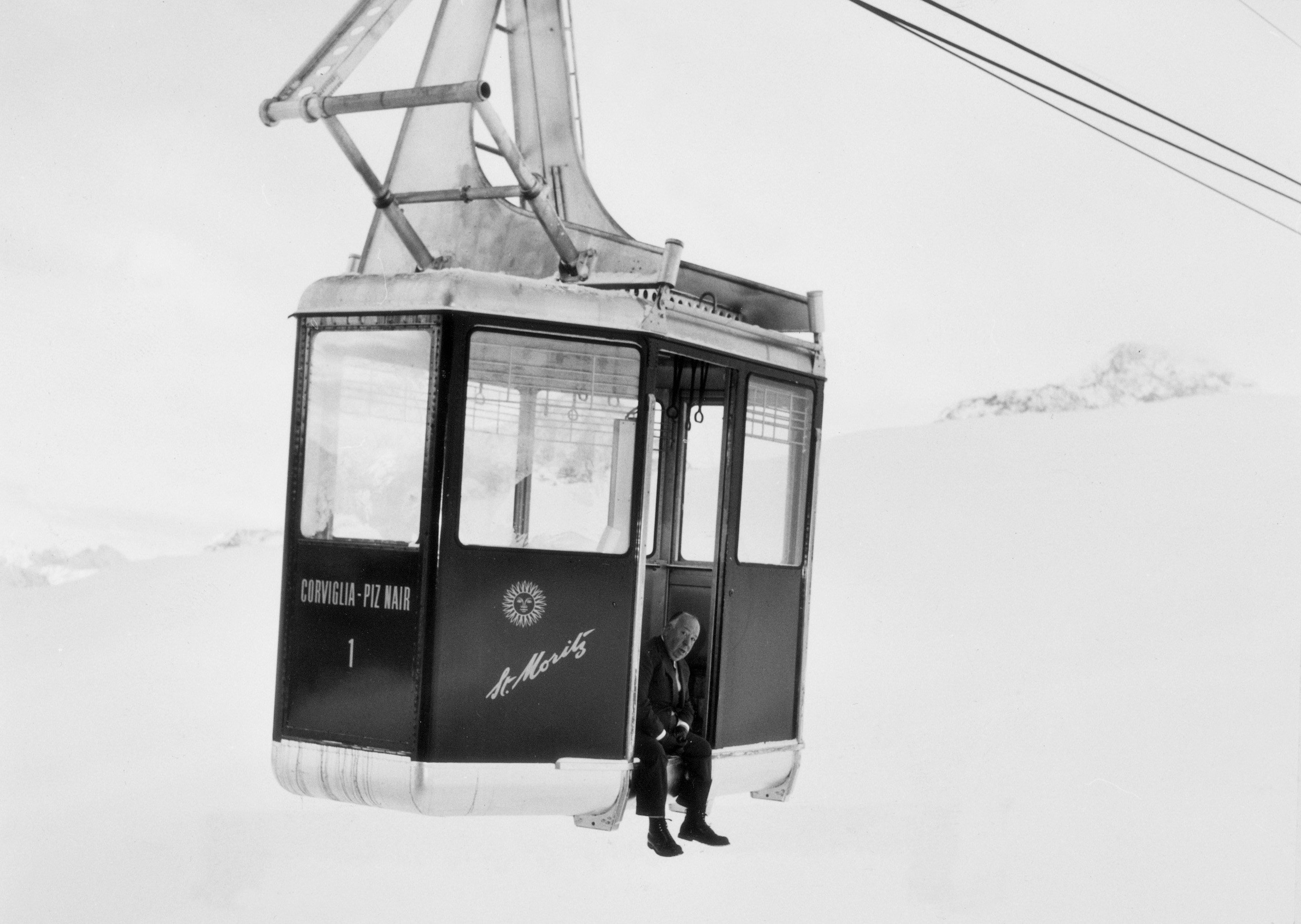 Alfred Hitchcock sitting by the open door of a teleferic, St. Moritz 1967