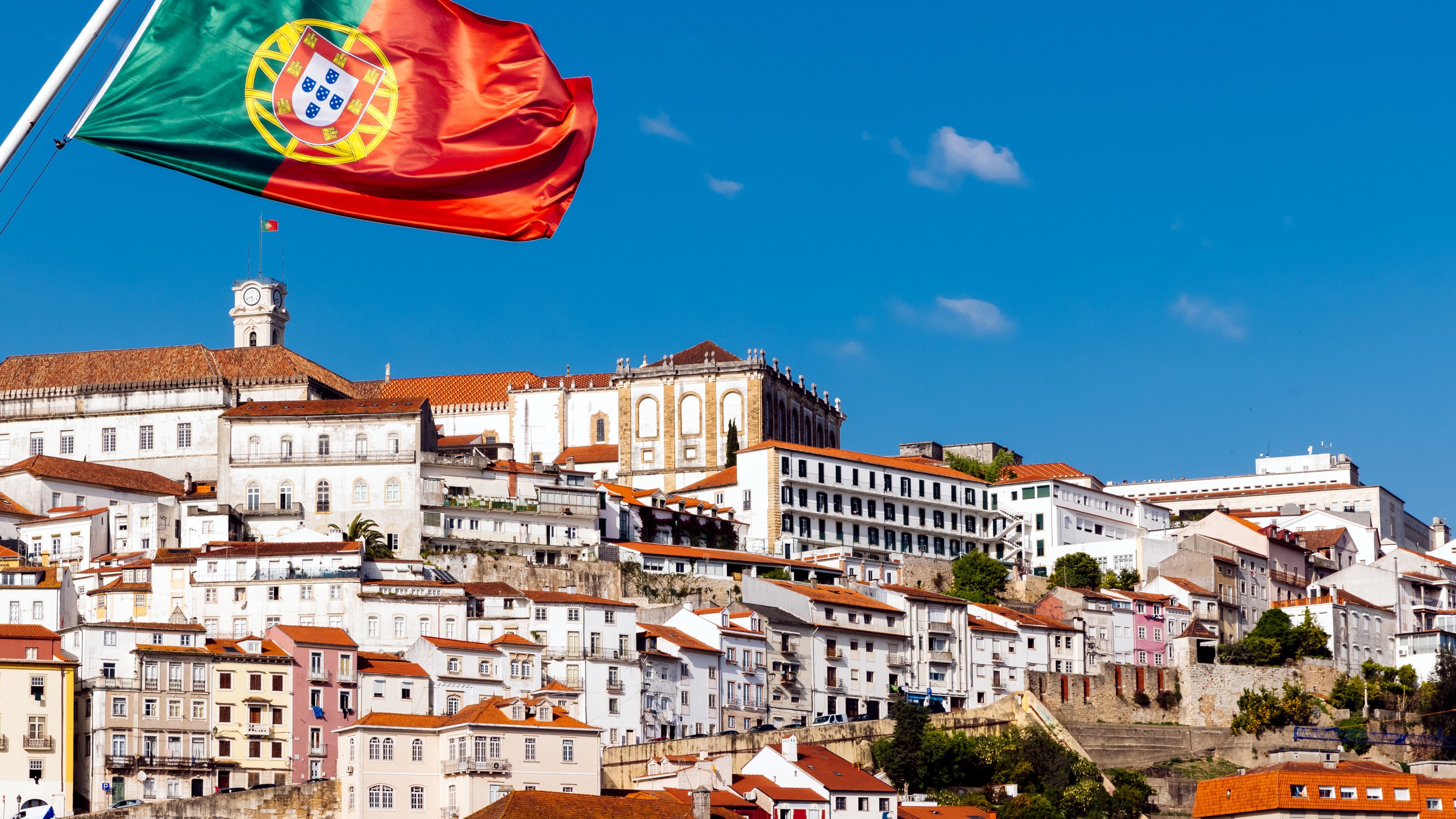 Portuguese flag waving in the wind and Coimbra skyline on a sunny day, Portugal