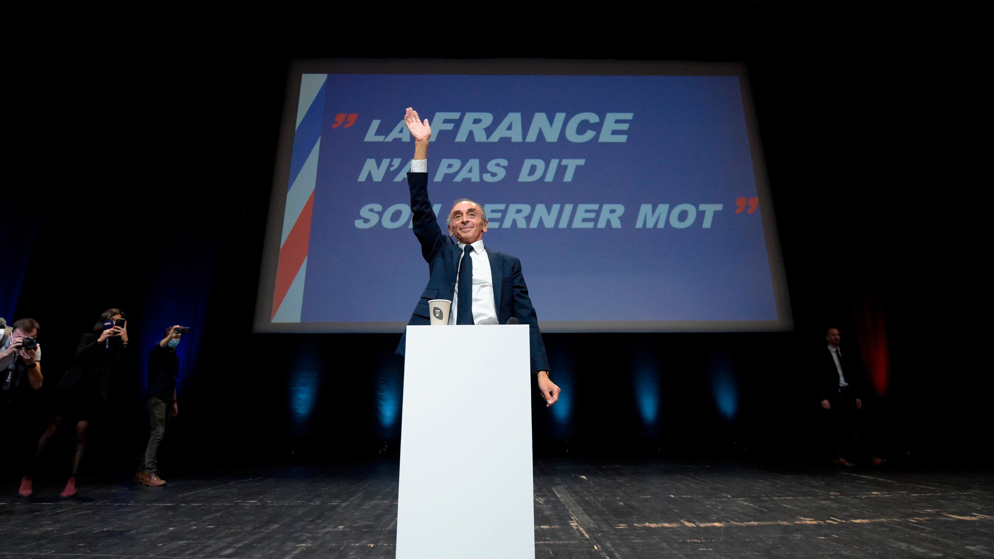 Eric Zemmour is seen on the stage with the title of his book